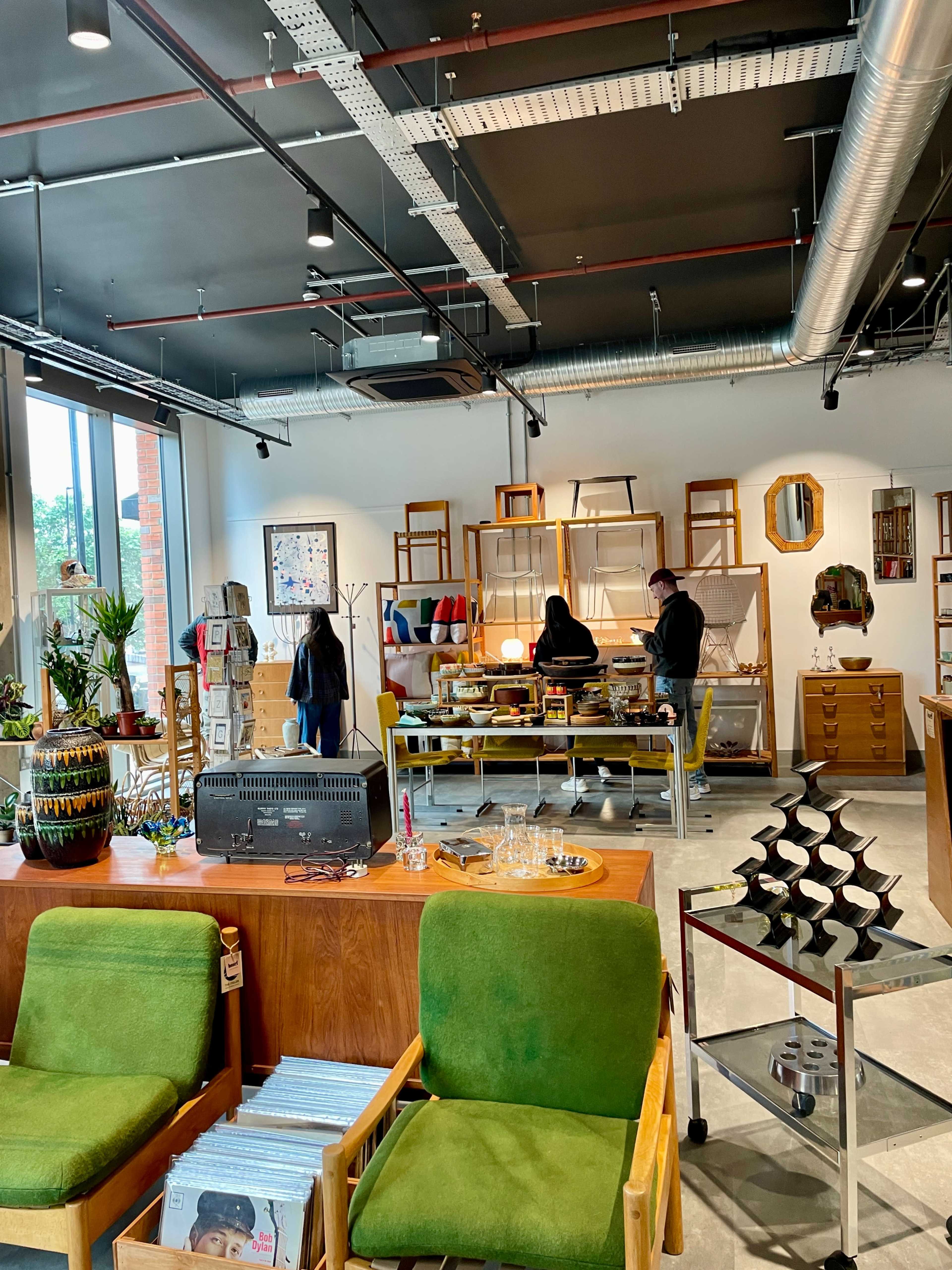 The image shows a modern retail space featuring wooden furniture, colorful decor, and two individuals interacting near a display table.
