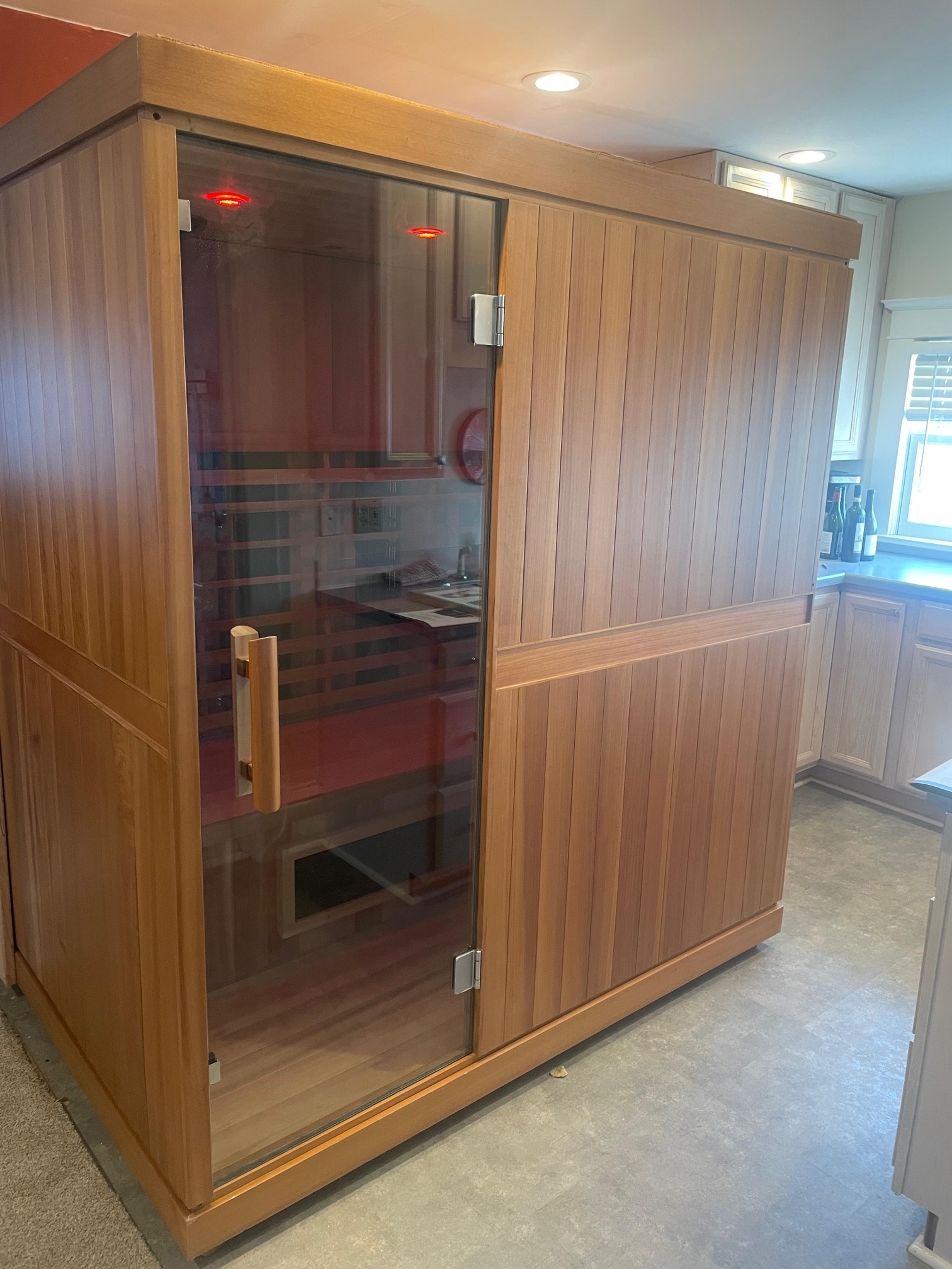 A wooden sauna with a glass door is positioned in a kitchen space.