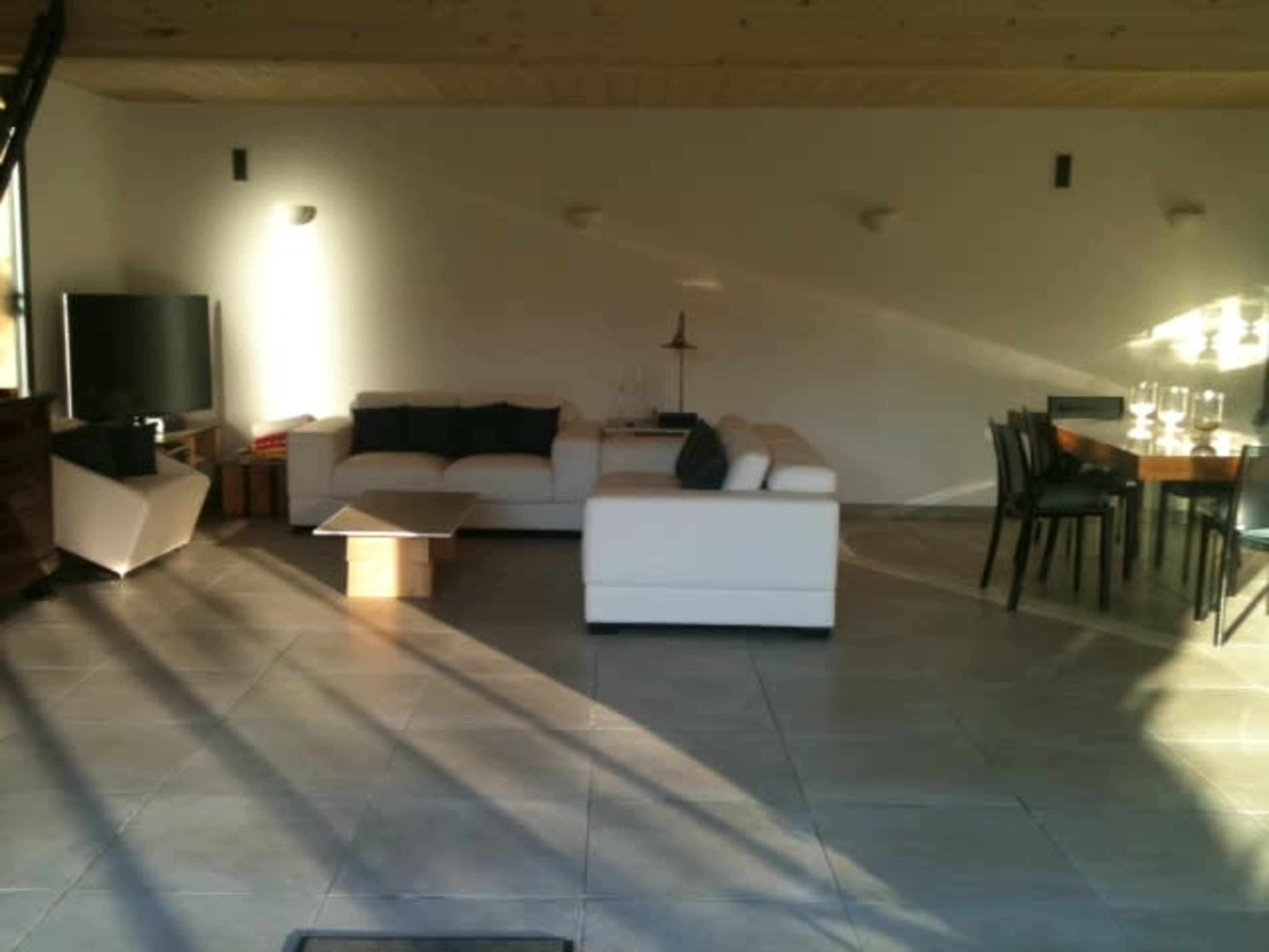 A modern living space with a white sectional sofa, a coffee table, a television, and a dining table with chairs.