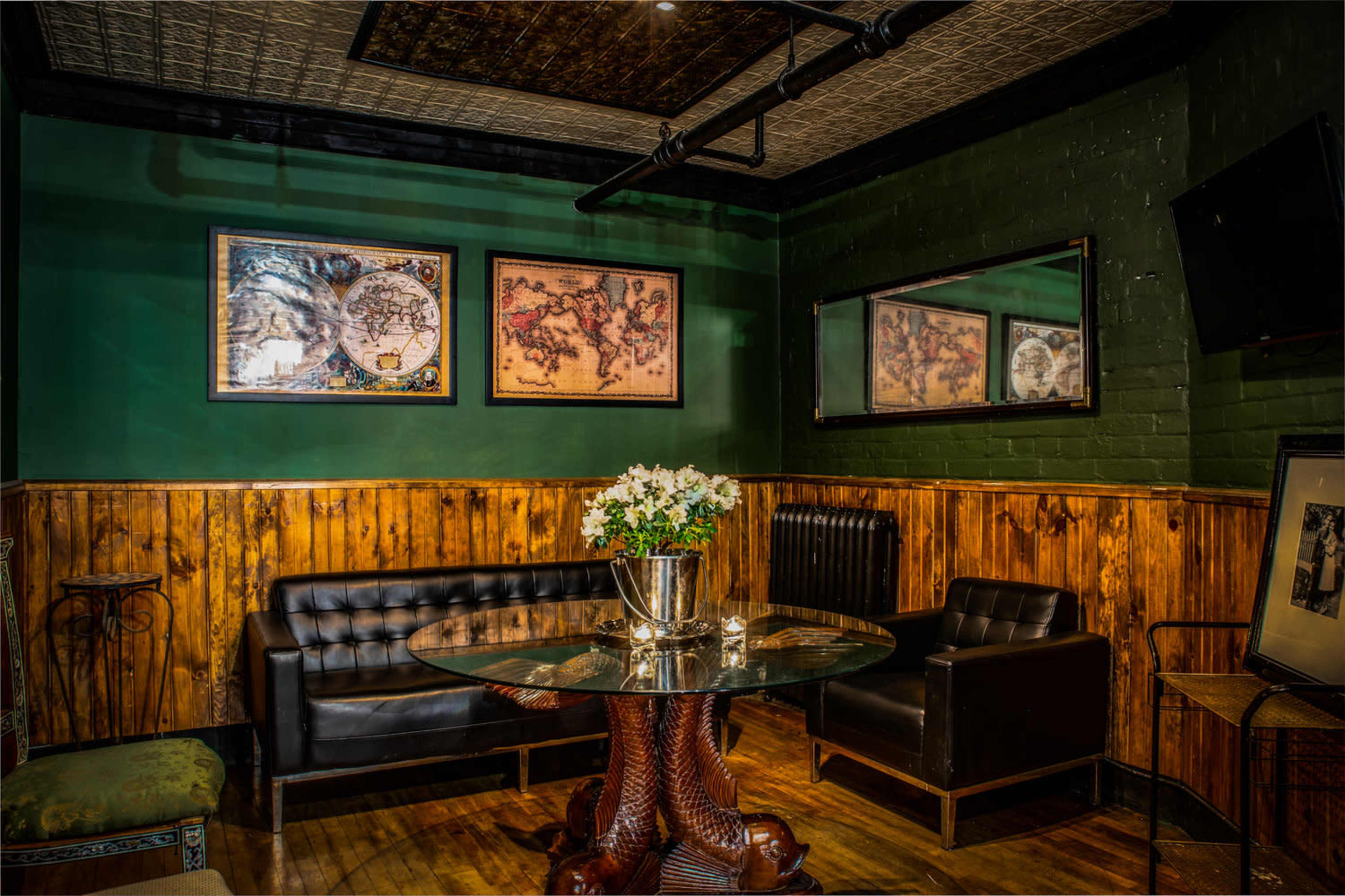A cozy lounge area with dark wood paneling, a glass table, and framed maps on the green walls.
