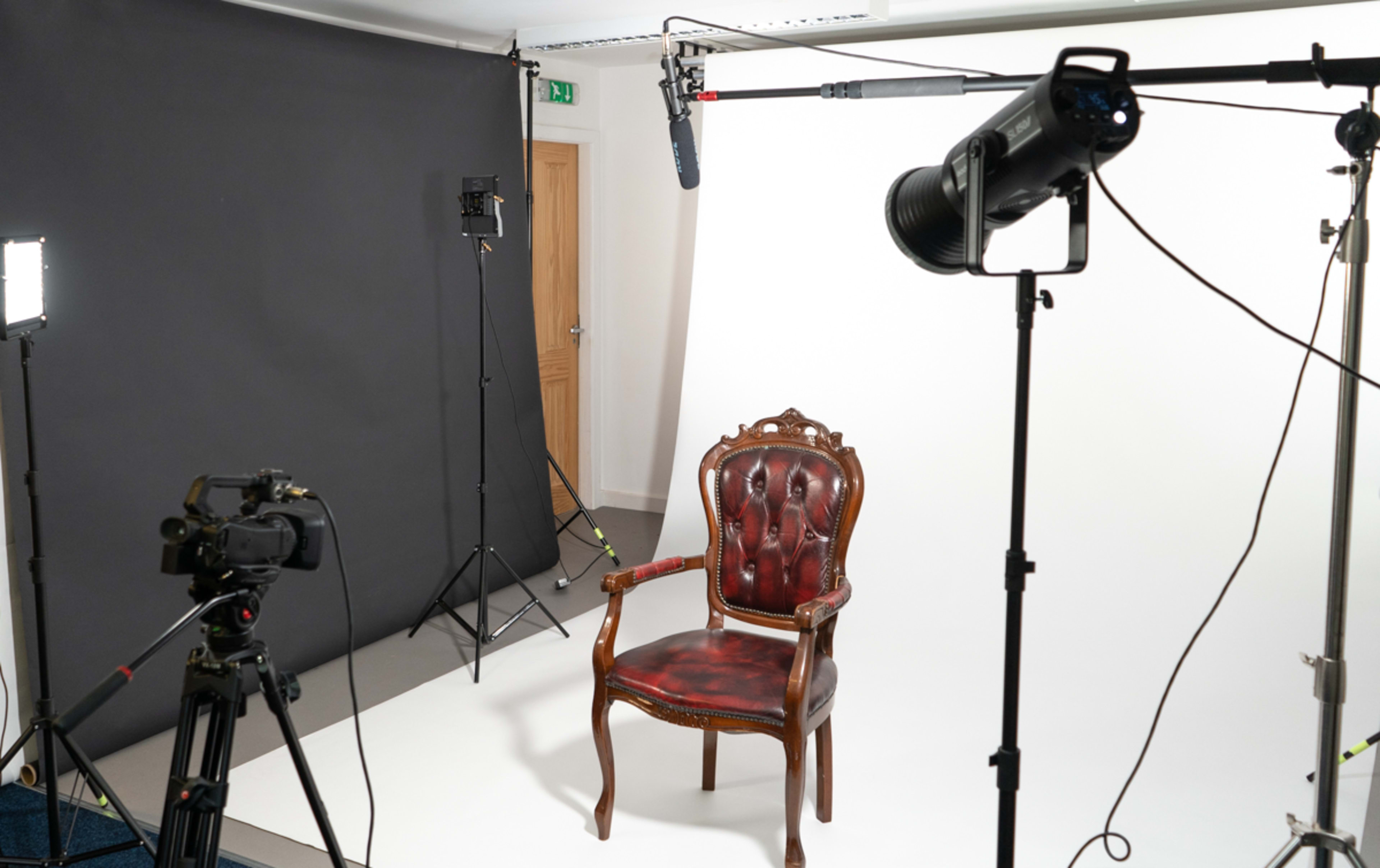 A vintage wooden chair with red upholstery is positioned in a photography studio surrounded by lighting and camera equipment.