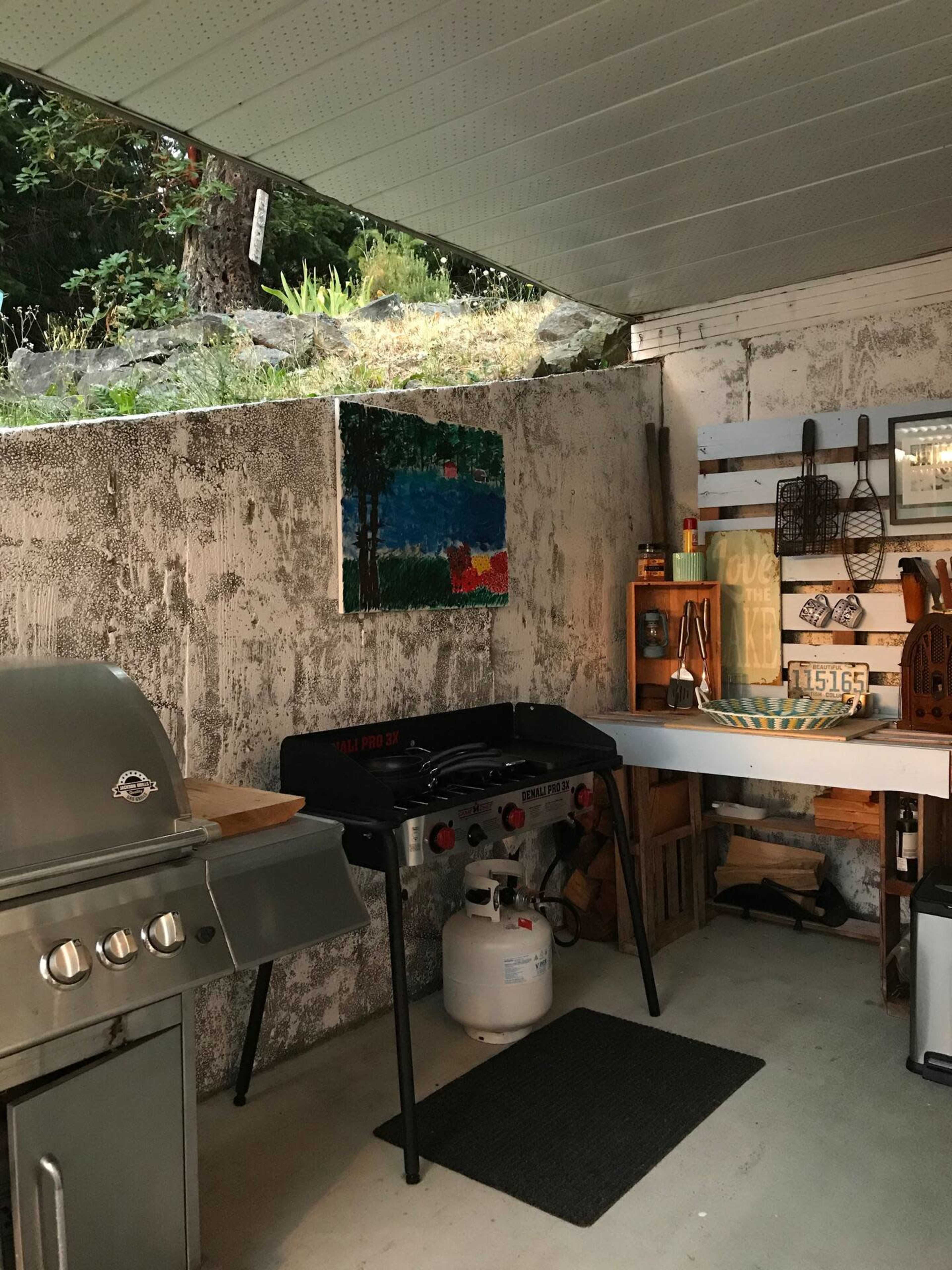 An outdoor kitchen area with a grill, sink, and various kitchen tools mounted on a wall, all enclosed by a concrete structure.
