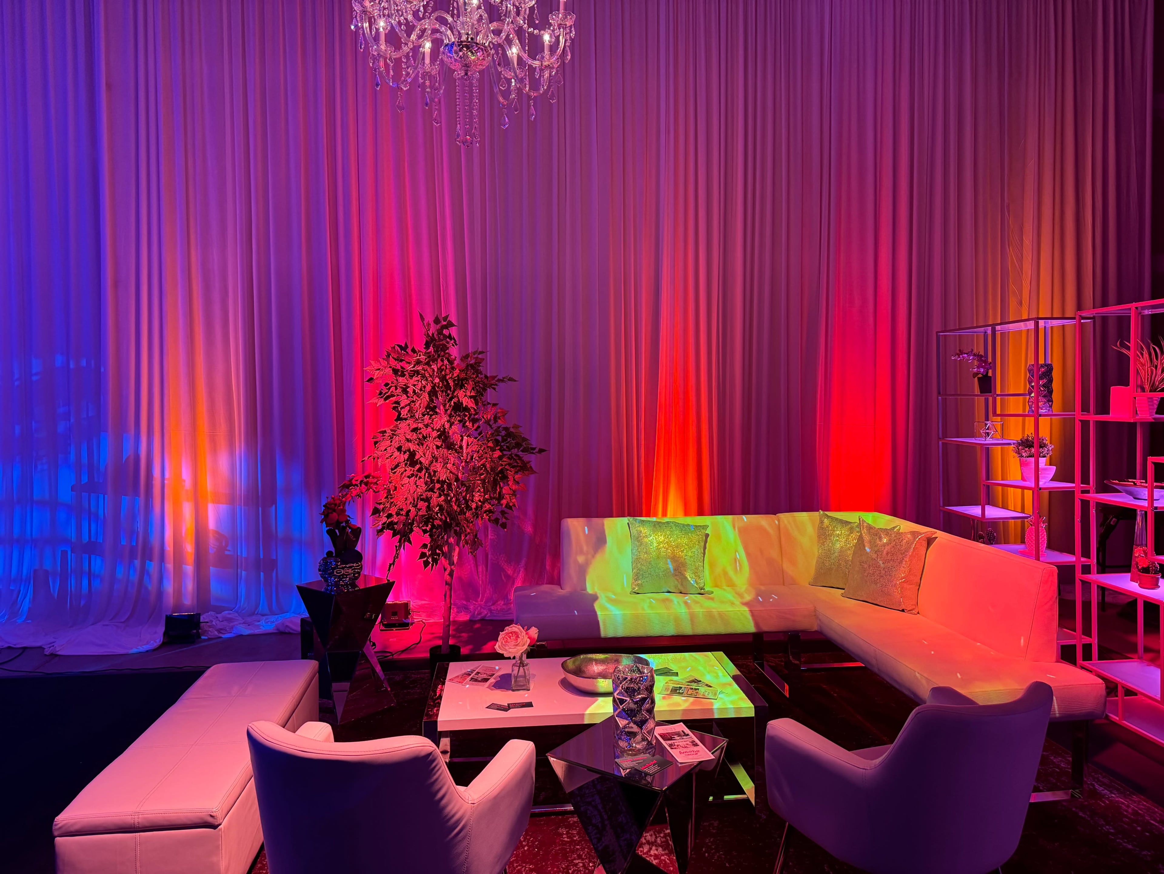 The scene features a modern lounge area with white furniture and colorful ambient lighting against a draped backdrop.