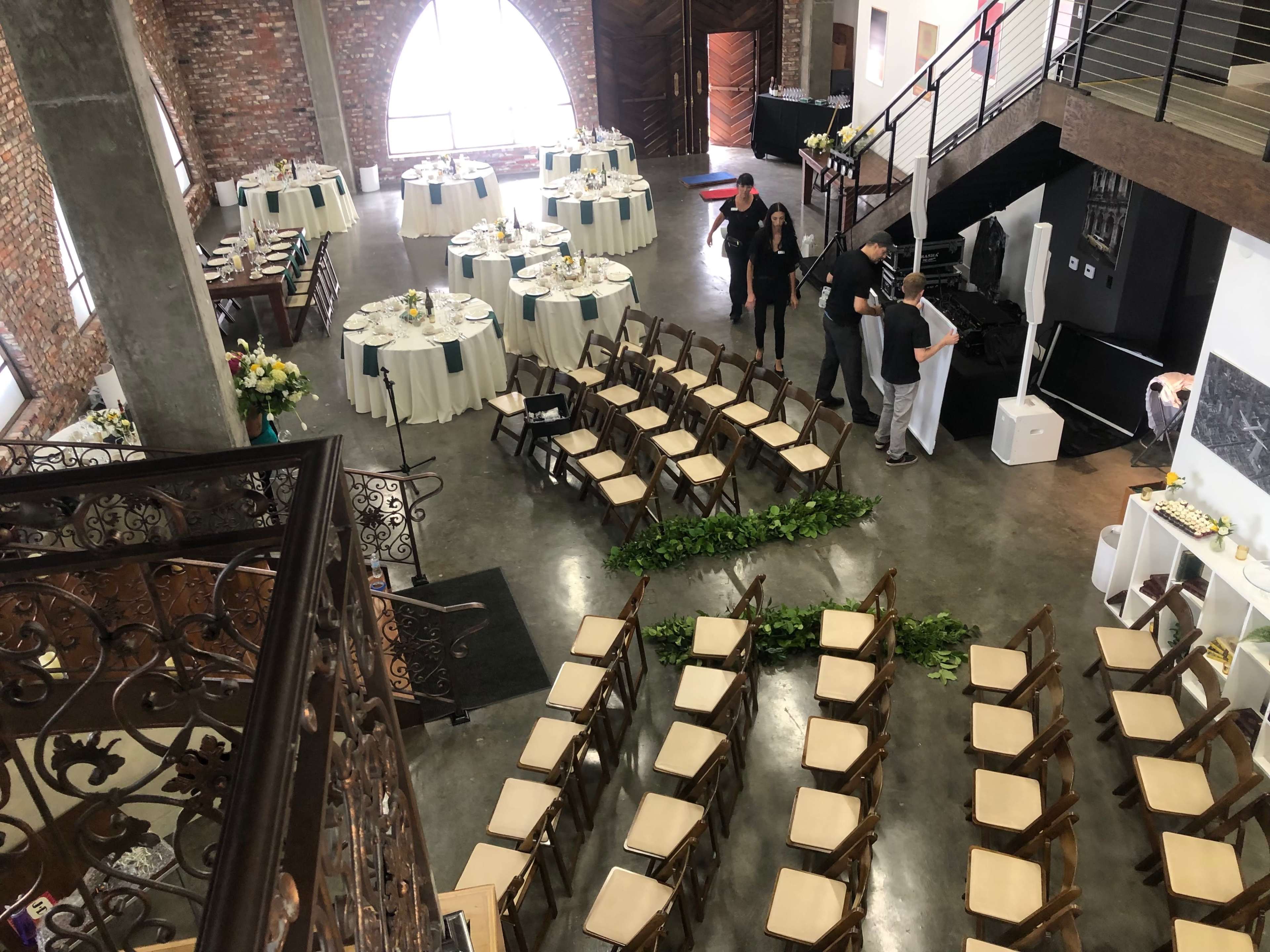 An elegantly arranged event space with tables set for dining and chairs lined up for a ceremony under a large arched window.