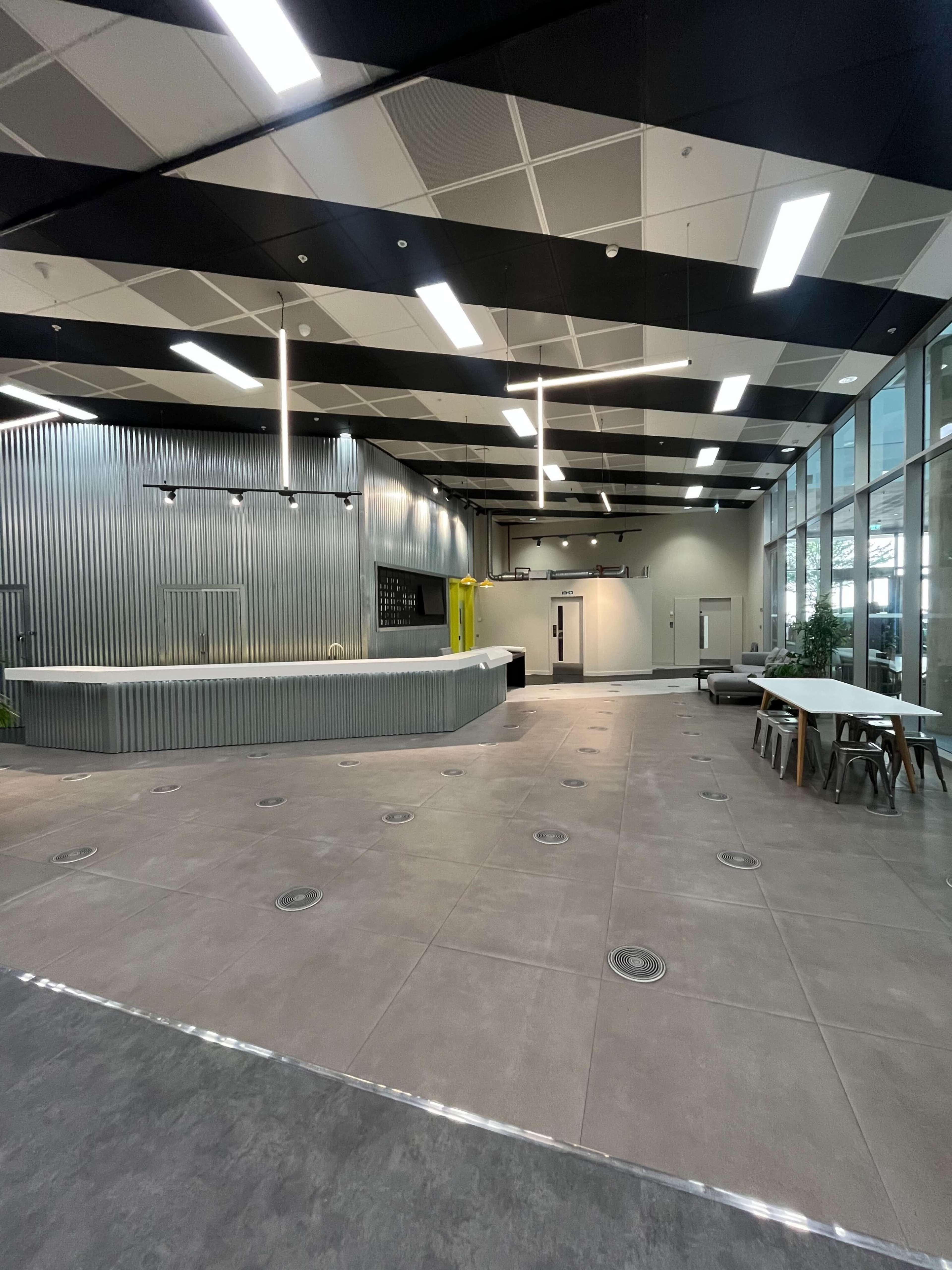 The image shows an open, modern reception area with a curved front desk, minimalist seating, and large windows allowing natural light.