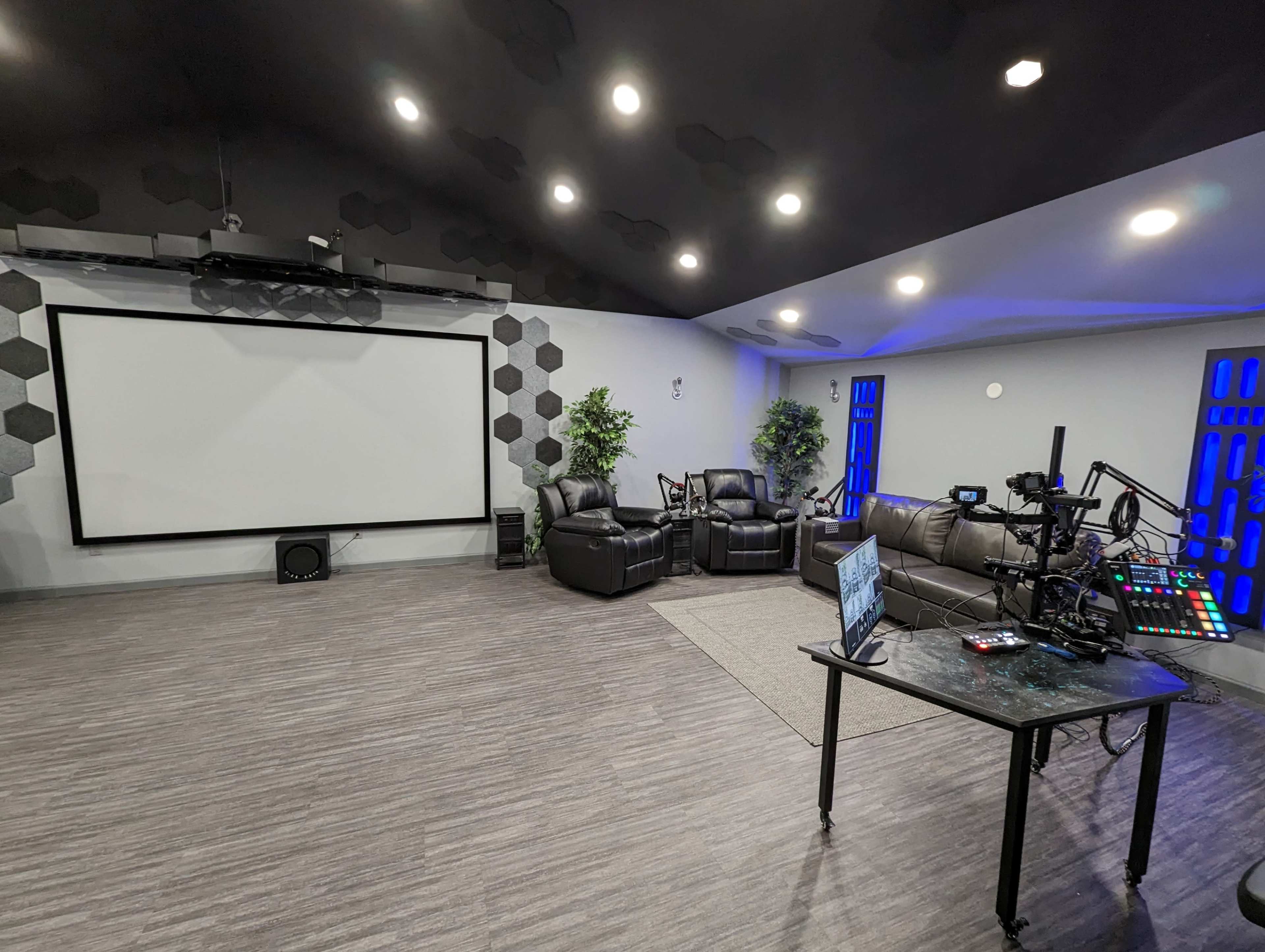 A modern home theater room with a large projection screen, dark leather seating, and a control desk equipped with audio-visual equipment.