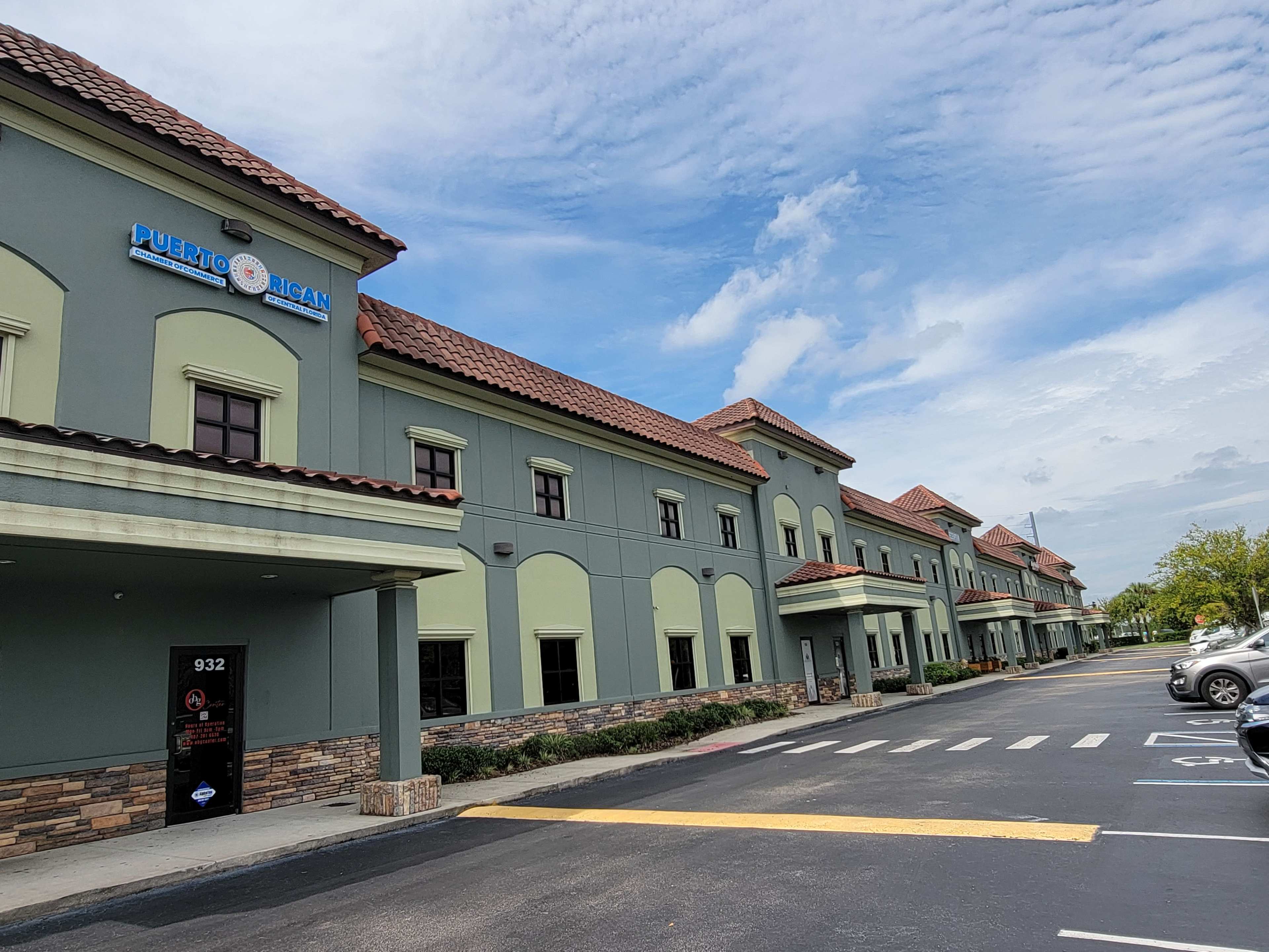 The image shows a green and beige building with a red tile roof, featuring signage for a Puerto Rican restaurant and a parking lot in front.