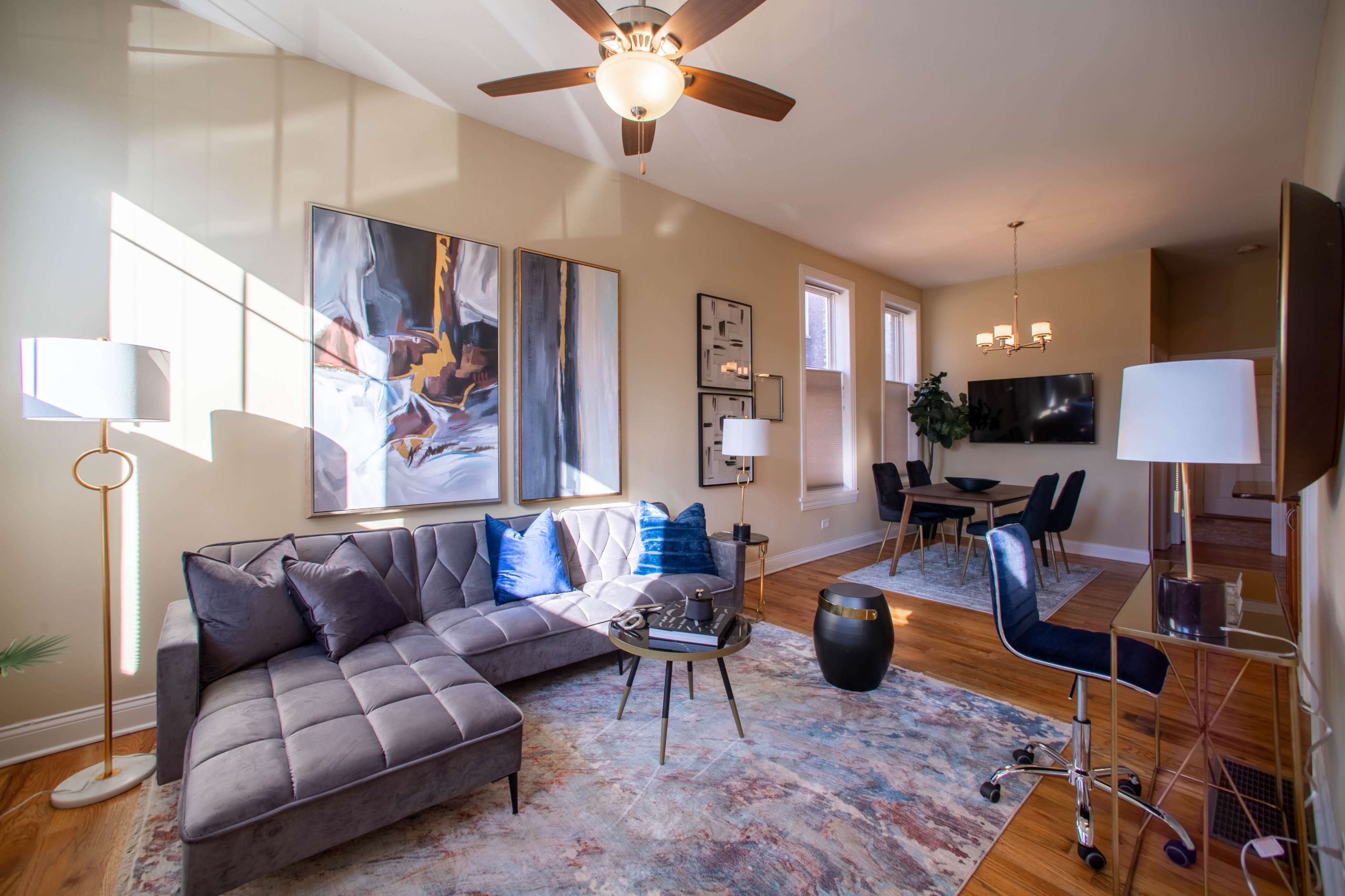 A modern living room with a sectional sofa, a circular coffee table, an artwork on the wall, and a dining area in the background.