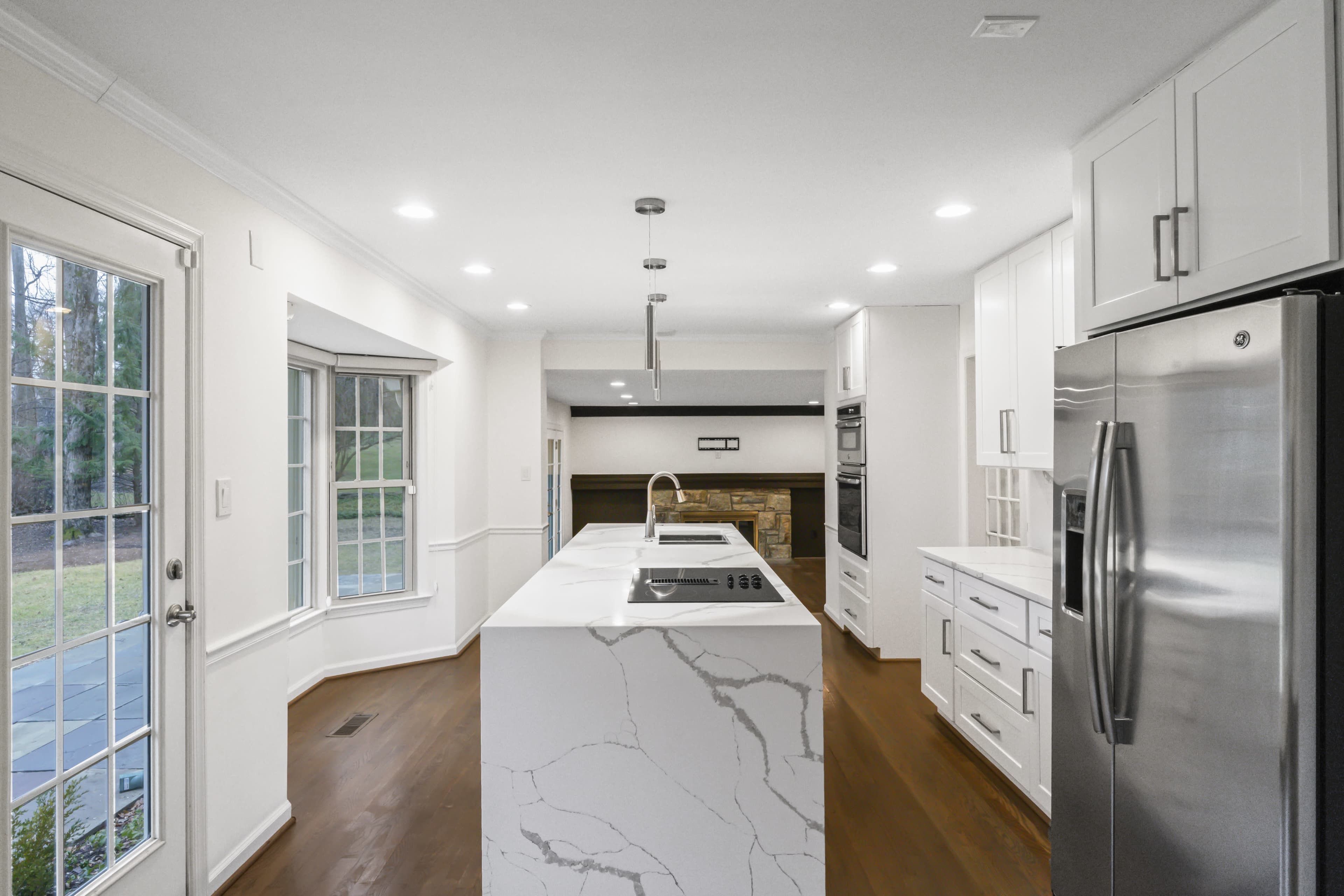 The image shows a modern kitchen with a large island, white cabinetry, and stainless steel appliances, featuring a spacious layout.