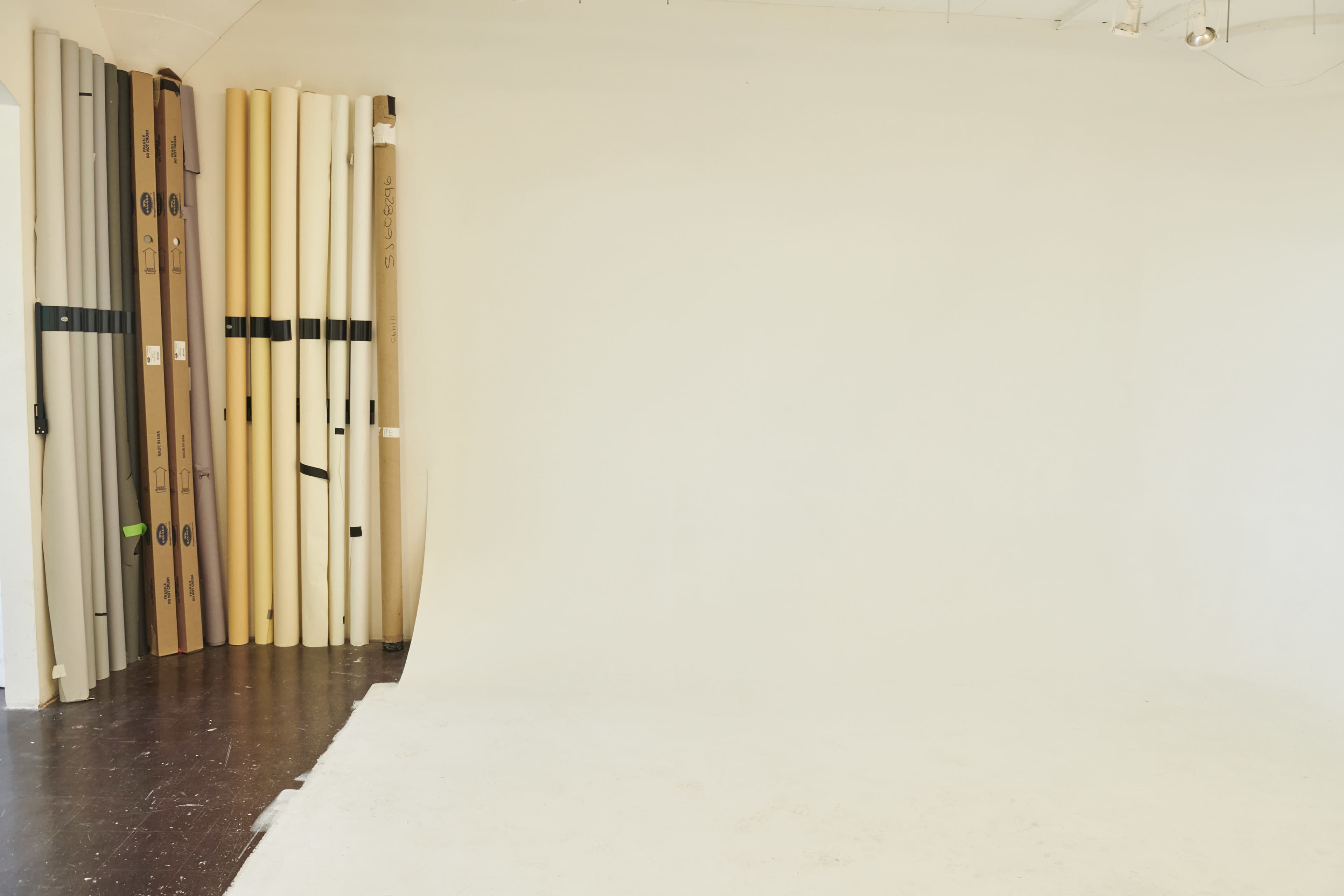 A photography studio features a white backdrop and rolls of backdrop paper arranged against a wall.