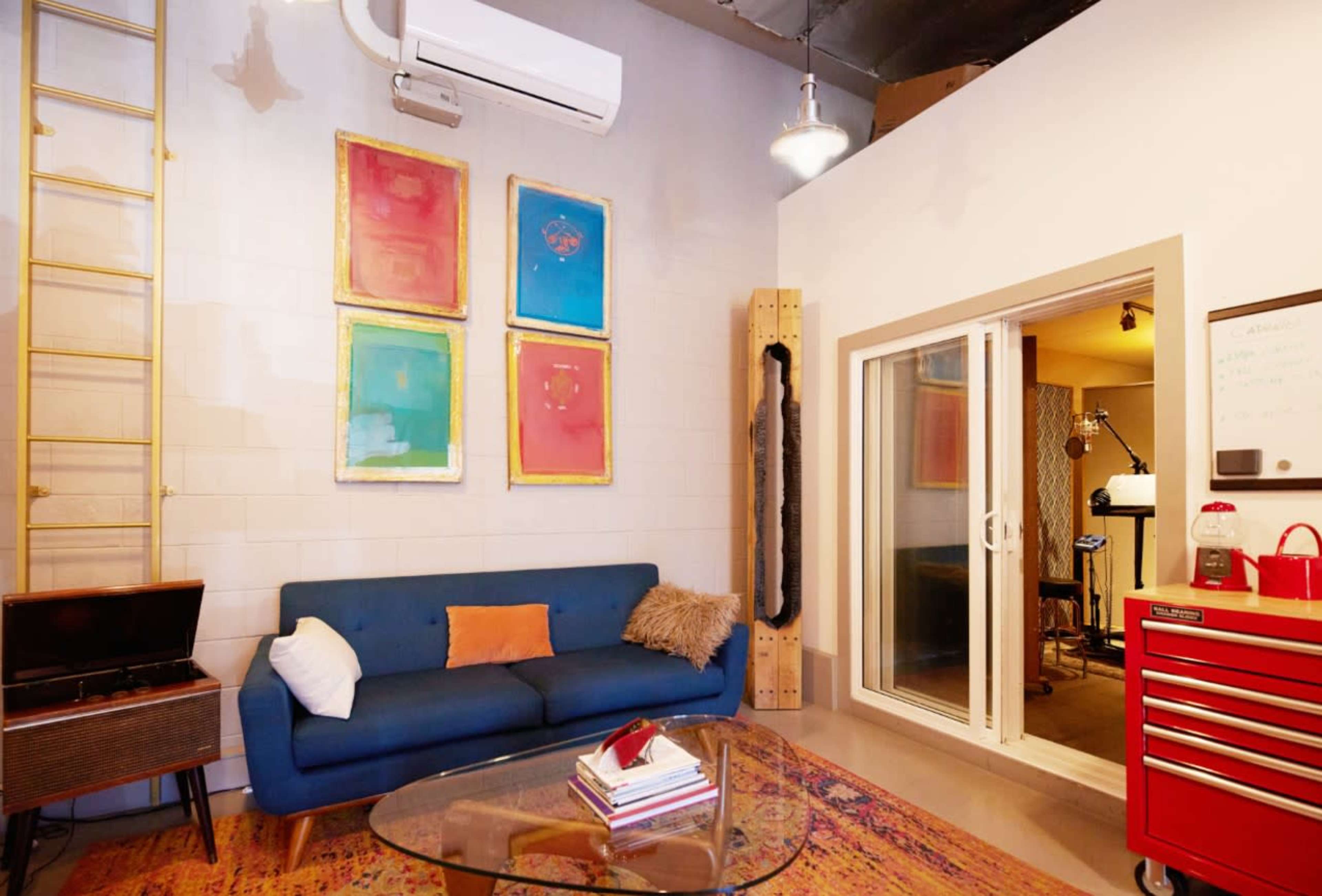 The image shows a modern room with a blue sofa, a glass coffee table, and colorful artwork on the wall, along with a tool chest and a partially closed glass door leading to another room.