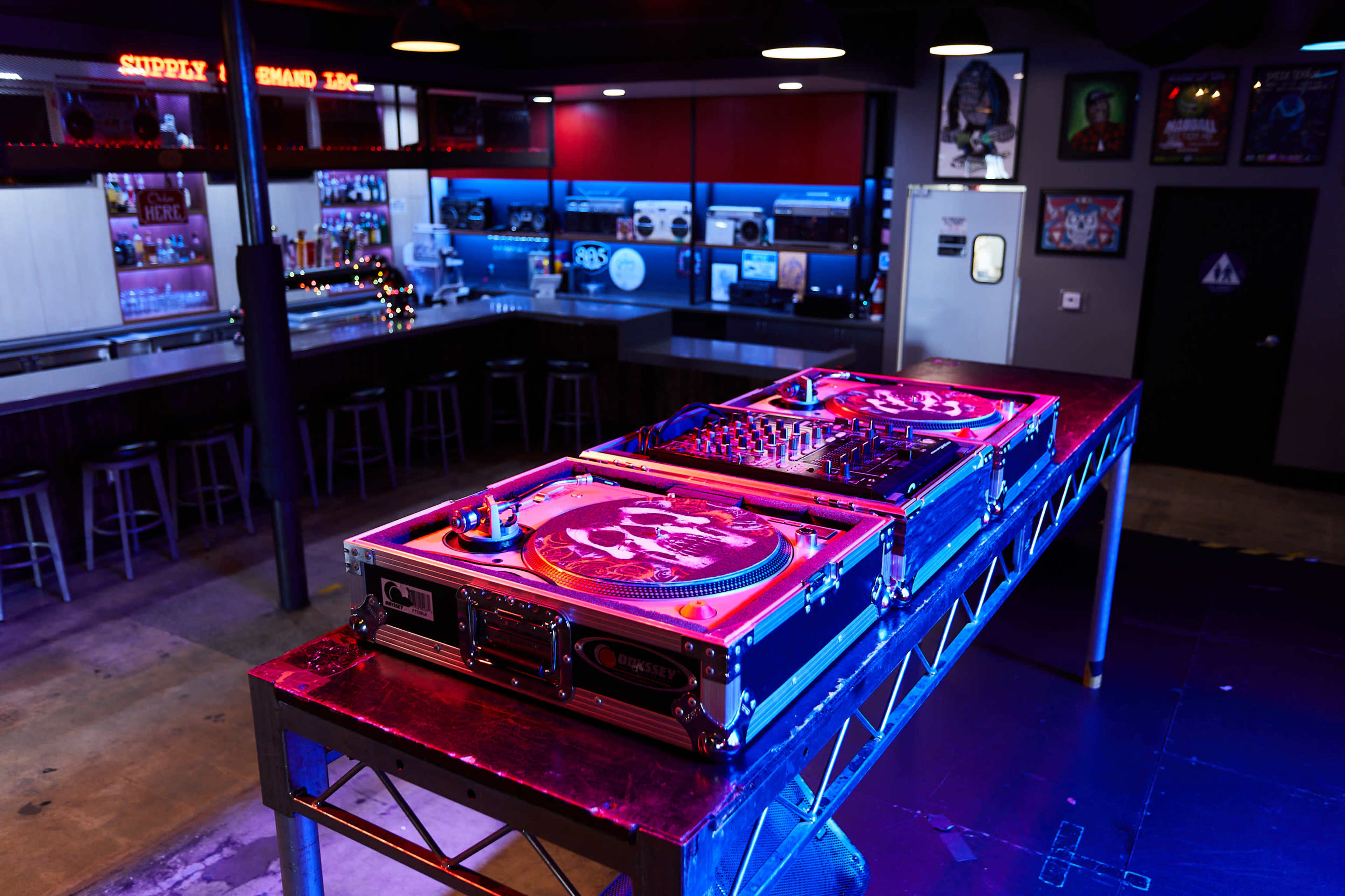 A pair of turntables and a mixer are set up on a metal table in a dimly lit bar with a modern design.