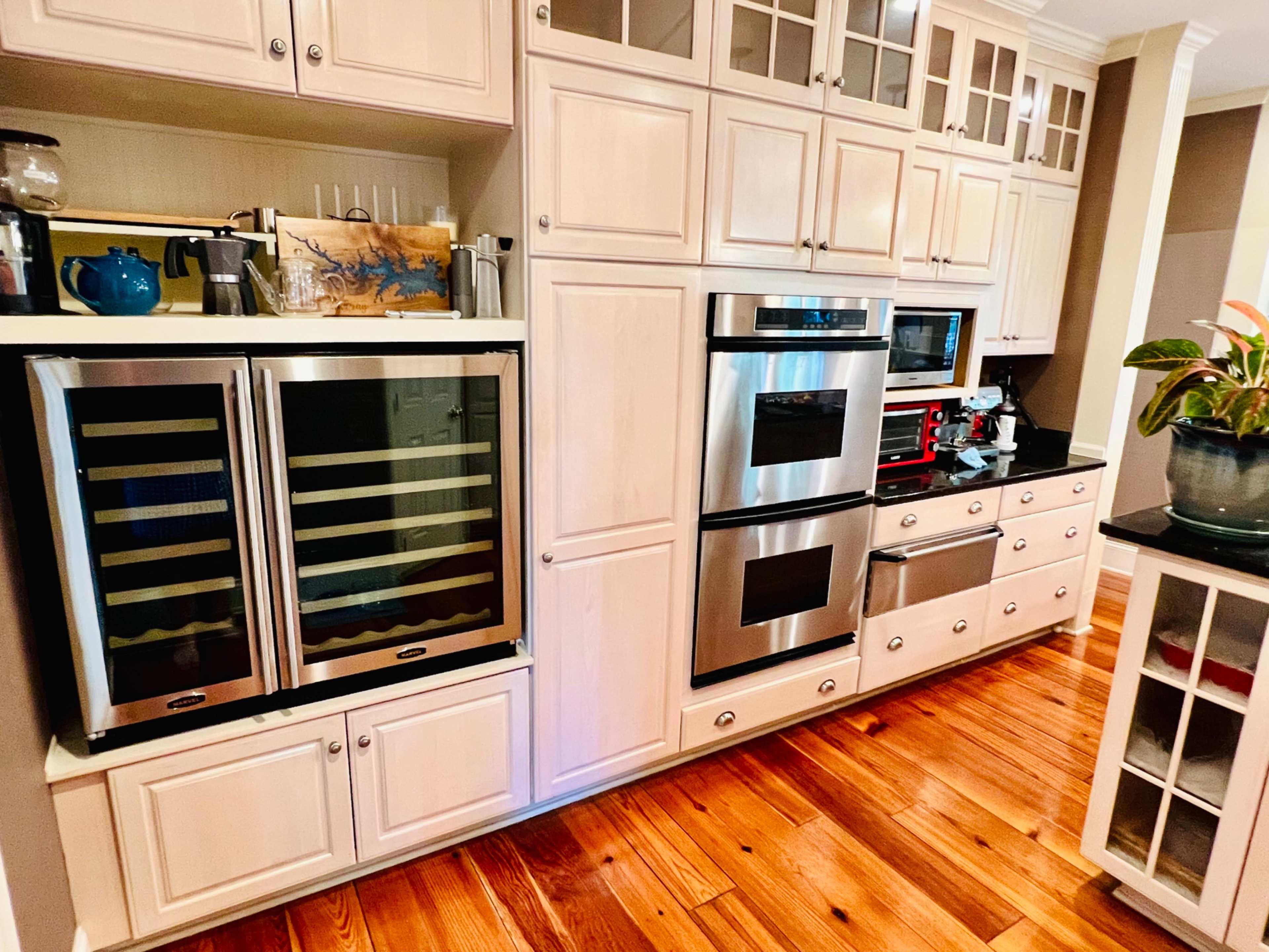 A modern kitchen with white cabinetry, stainless steel appliances, and wooden flooring.