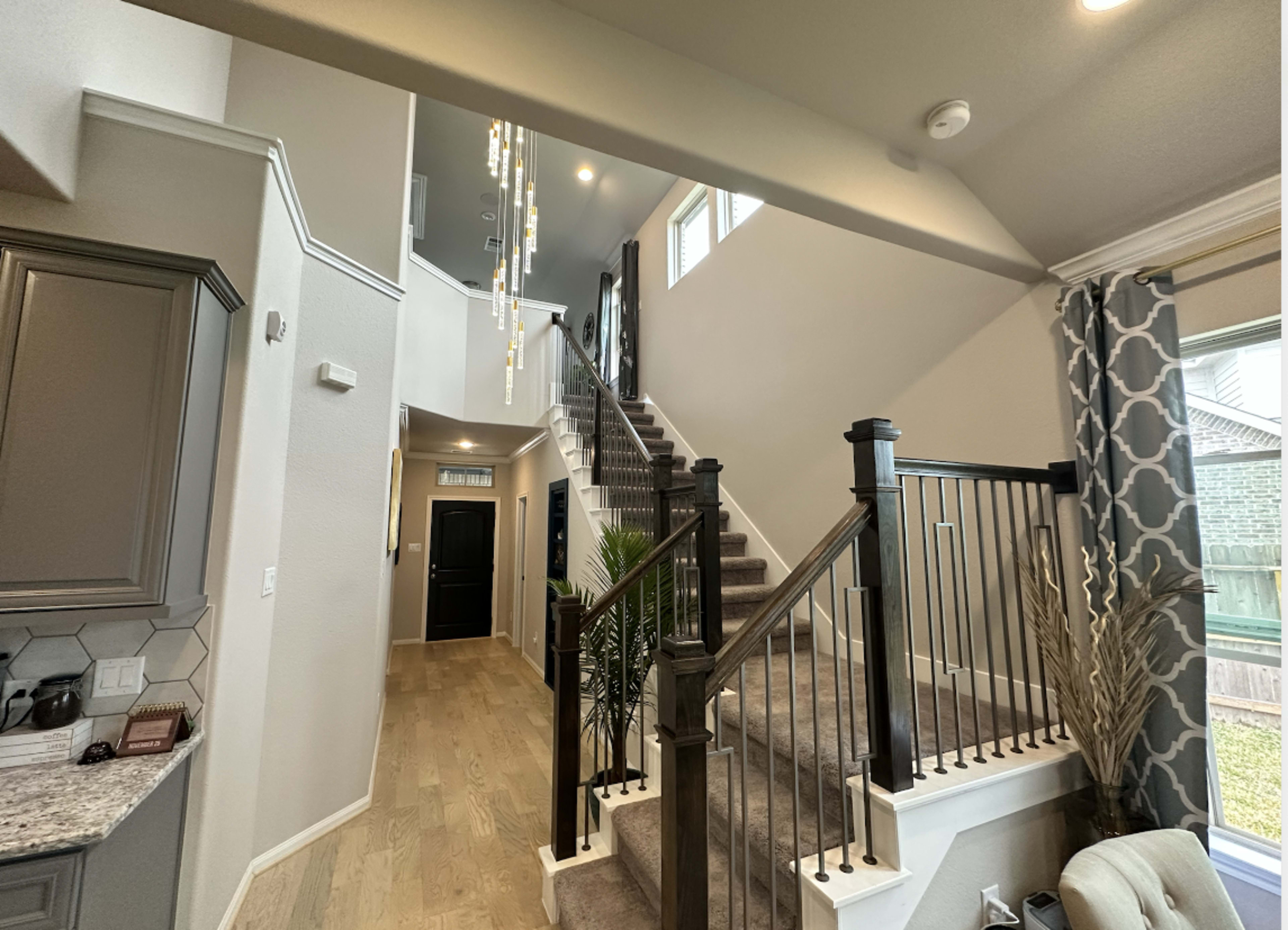 A modern entryway with a staircase leading to the upper floor, framed by walls painted in light colors and decorated with a pendant light fixture.