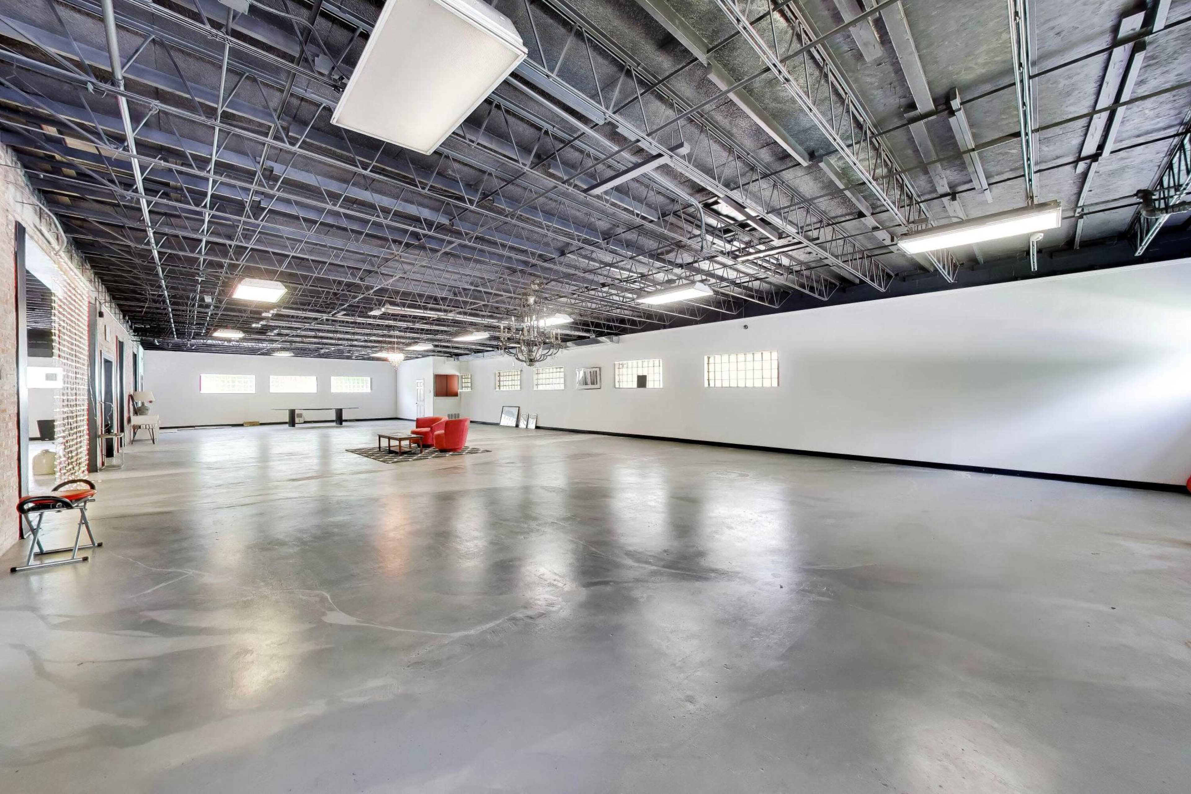 The image shows a large, empty commercial space with concrete flooring, high ceilings, and minimal furnishings.