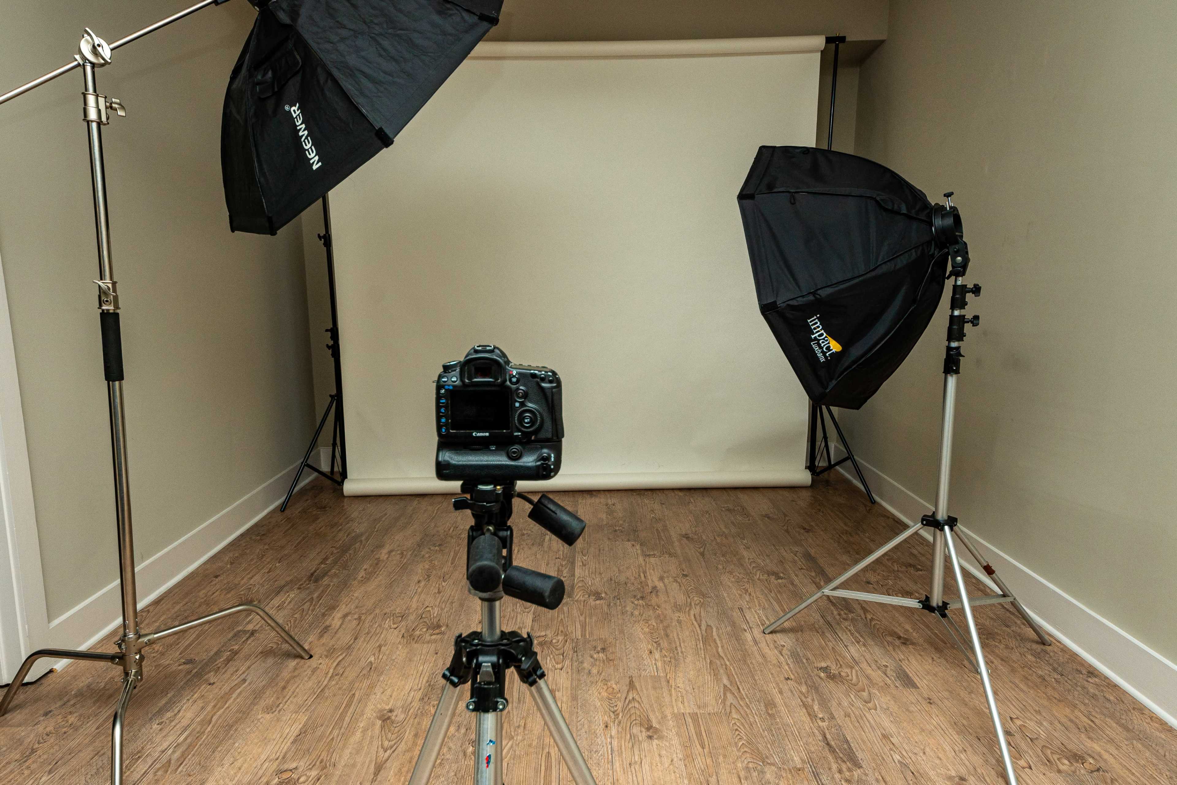 A camera is positioned on a tripod in front of a neutral backdrop, flanked by two lighting setups.