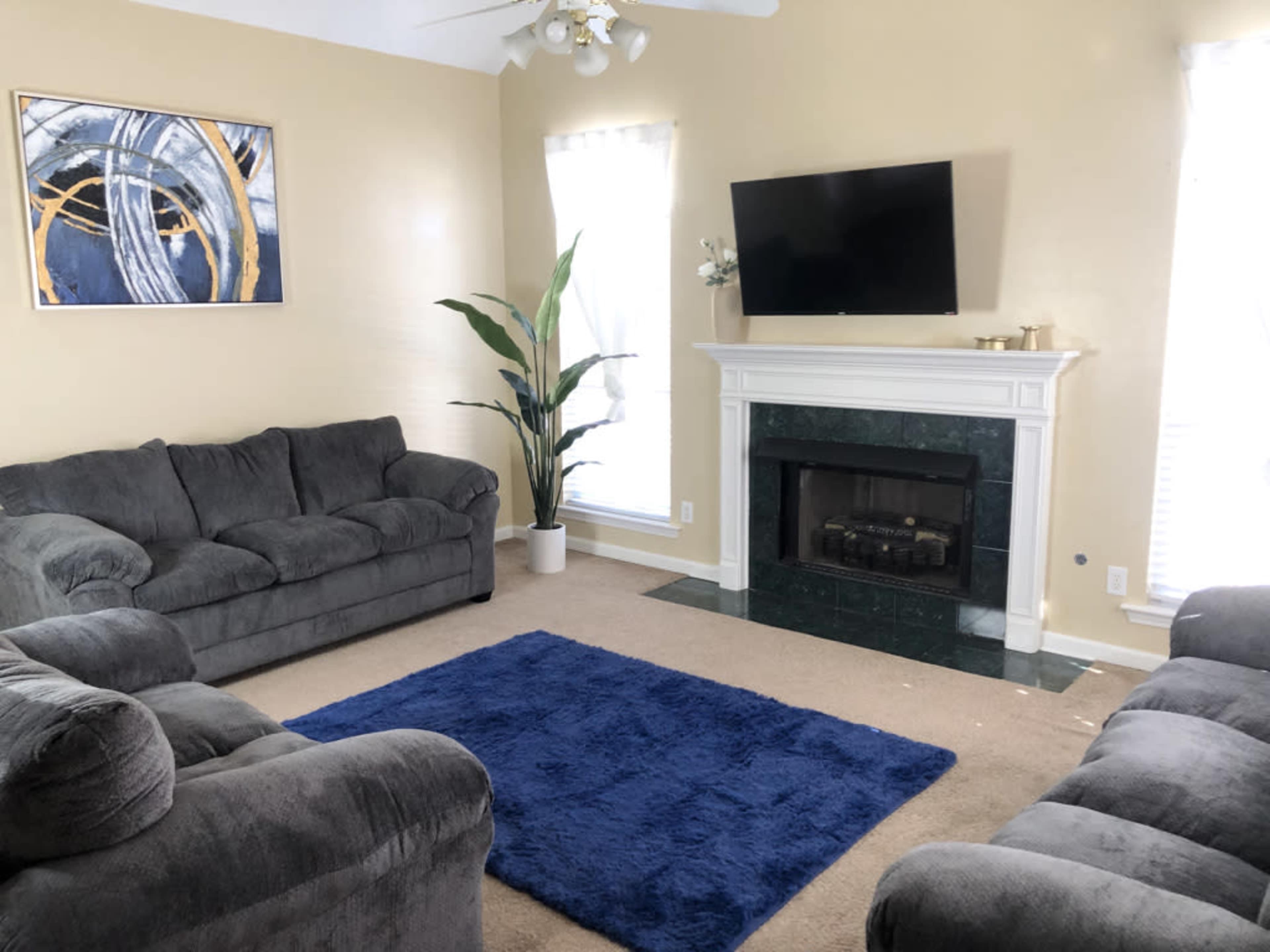 A living room with two gray sofas, a blue area rug, a marble fireplace, and a mounted television on a light yellow wall.