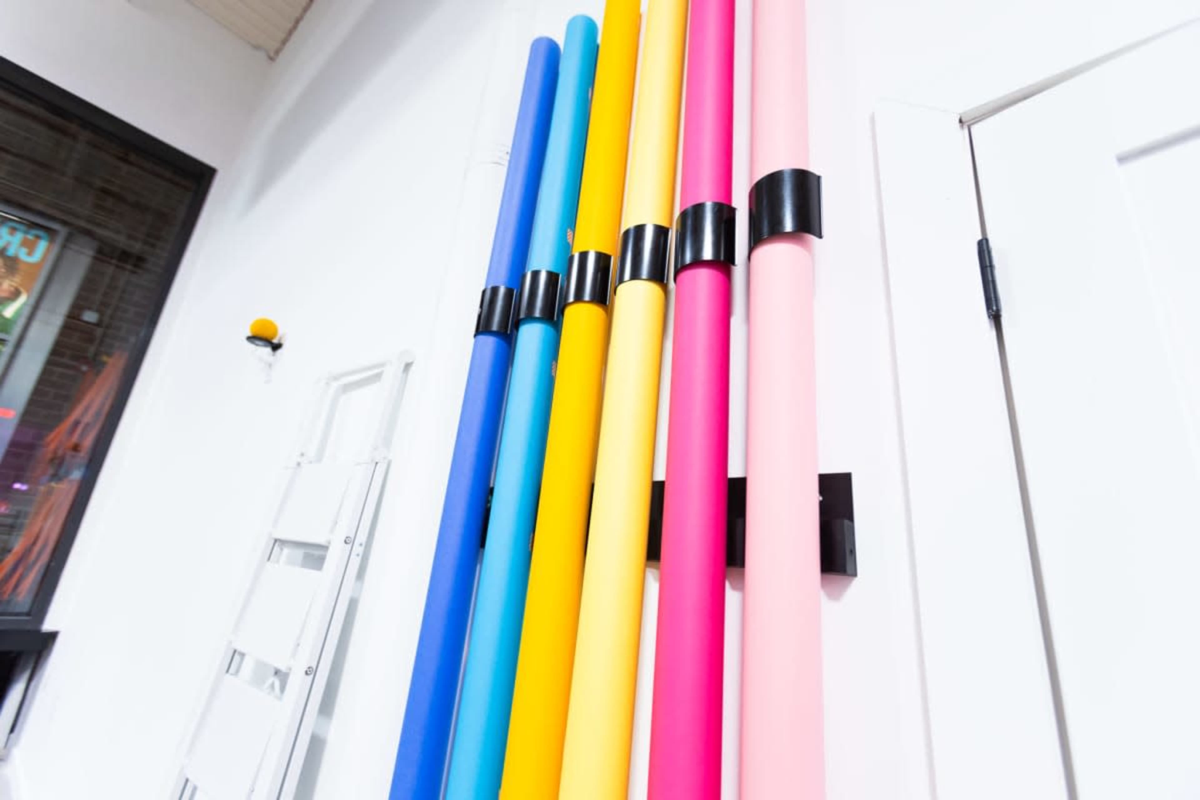 Colorful rolls of paper in blue, yellow, pink, and other shades are mounted vertically against a white wall.