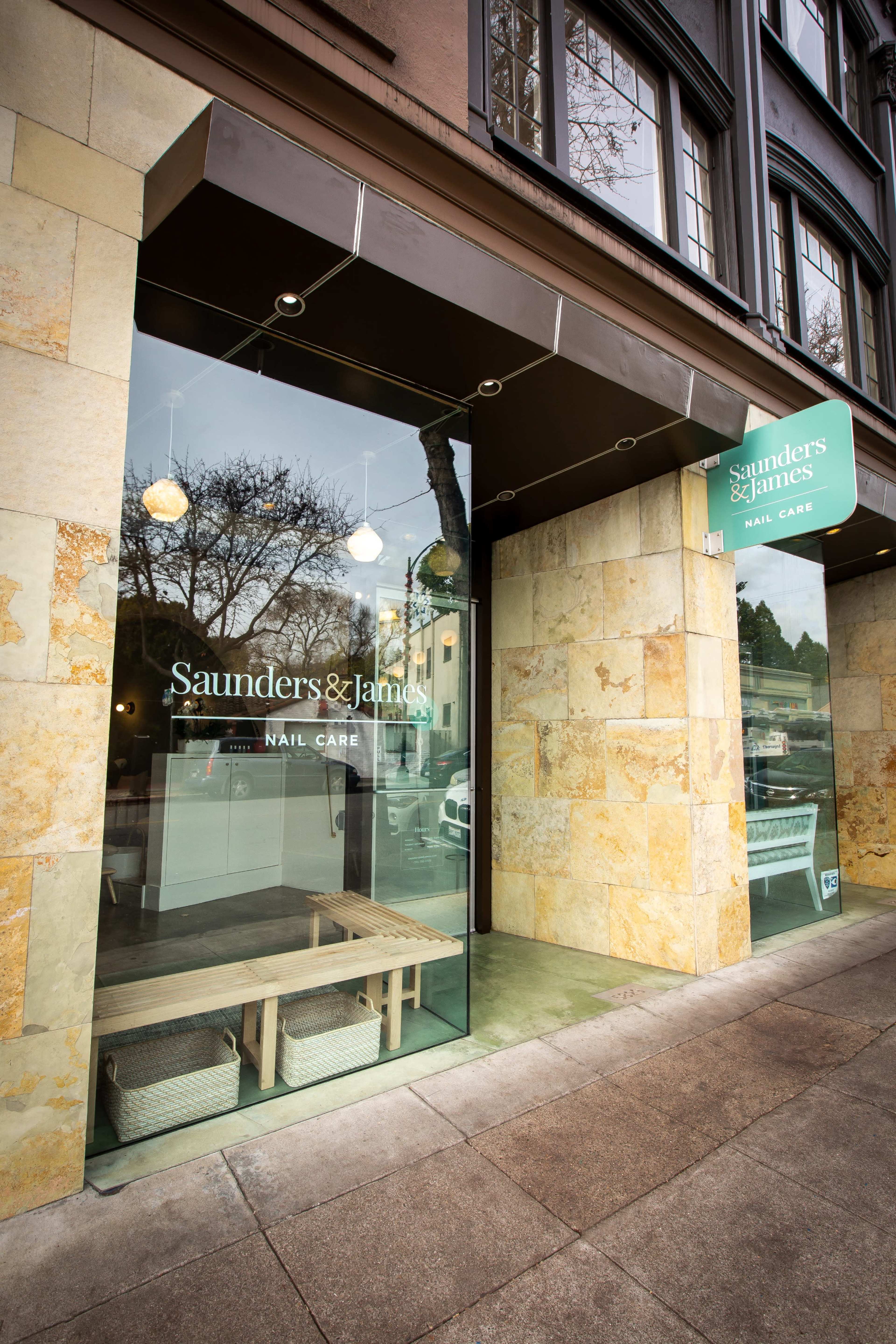 A storefront labeled "Saunders & James Mail Care" with a glass entrance and a stone exterior.