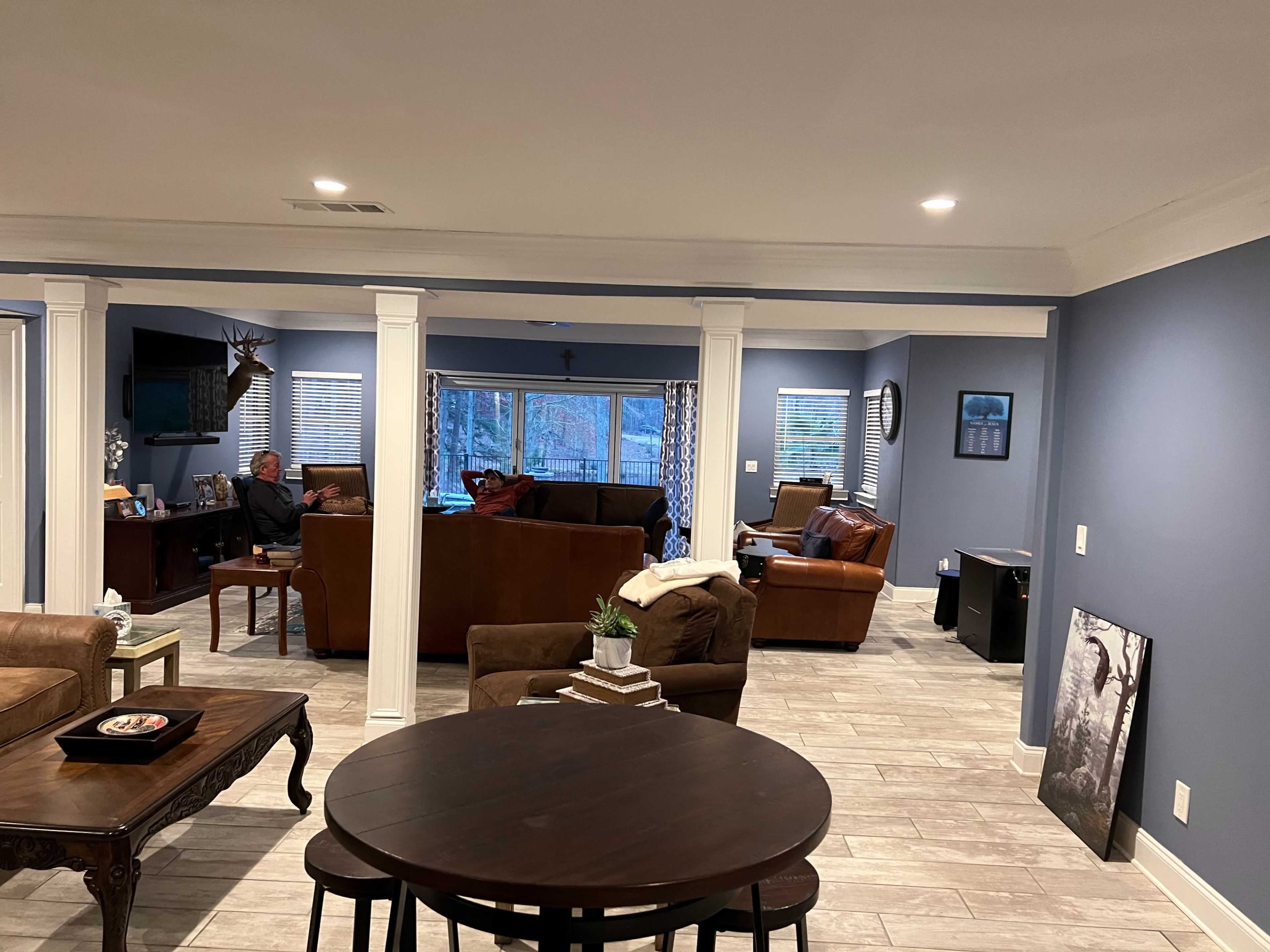 A spacious living room area with two seating areas, light-colored walls, and large windows overlooking an outdoor space.
