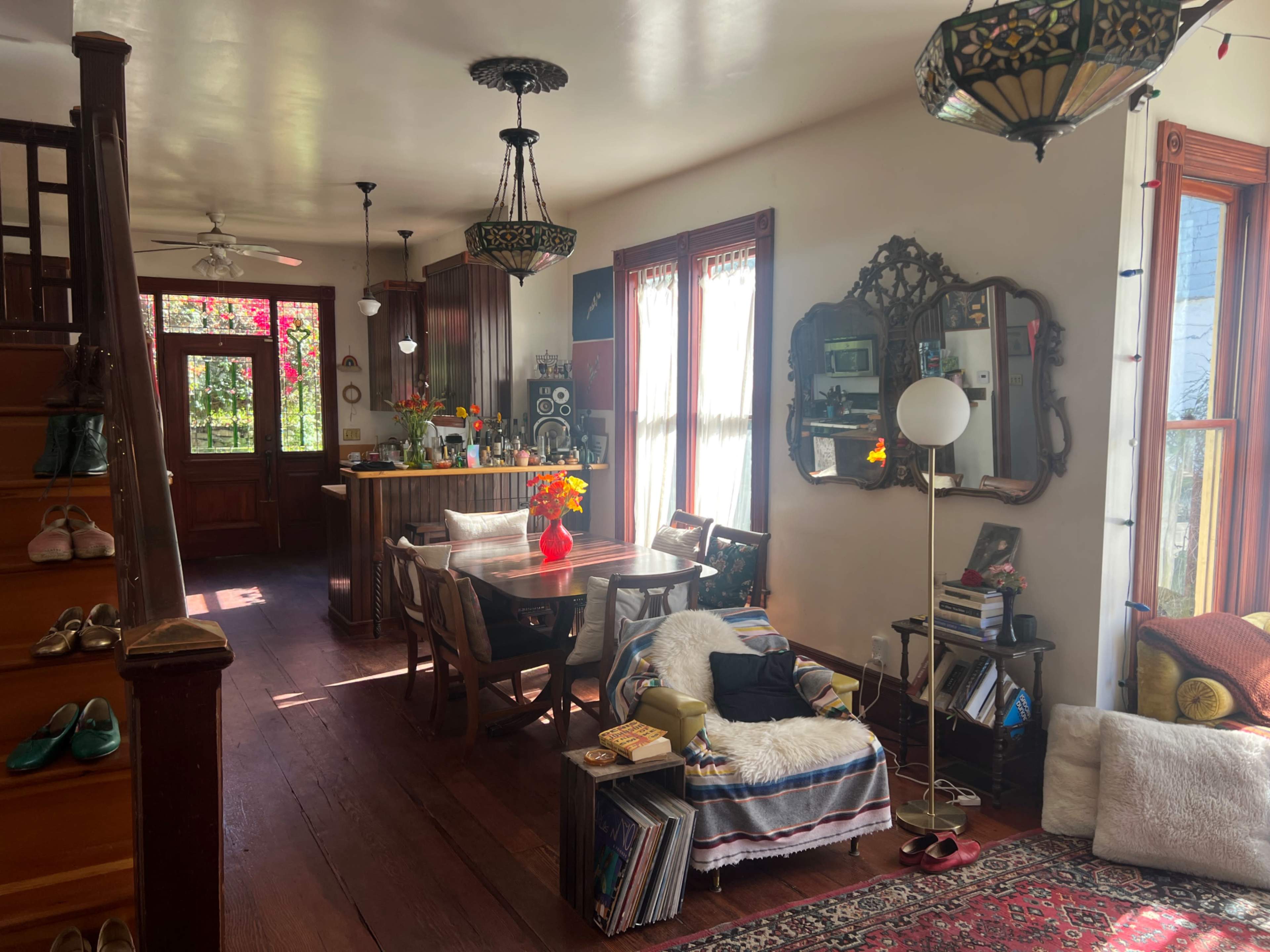 The image shows a cozy living area with a dining table, a kitchen in the background, and decorative lighting fixtures.