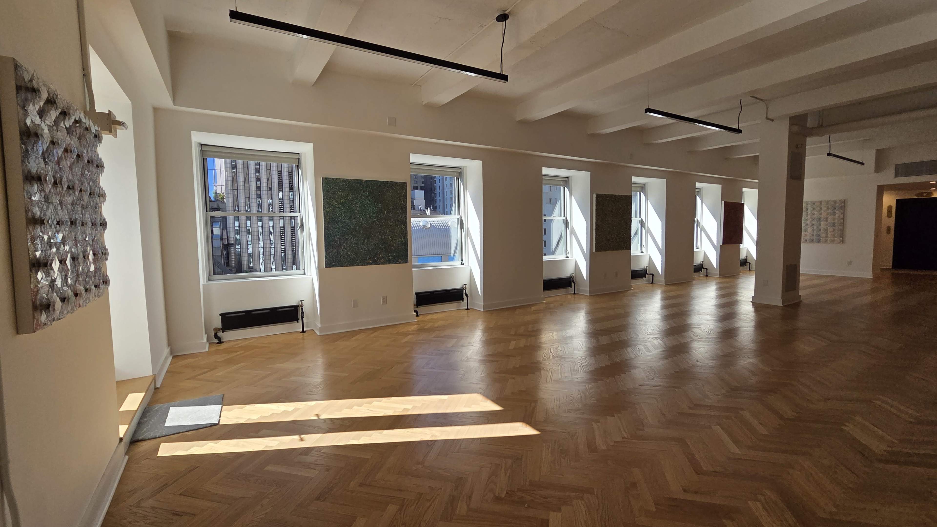 The image shows a bright, spacious room with large windows and several pieces of artwork displayed on the walls.