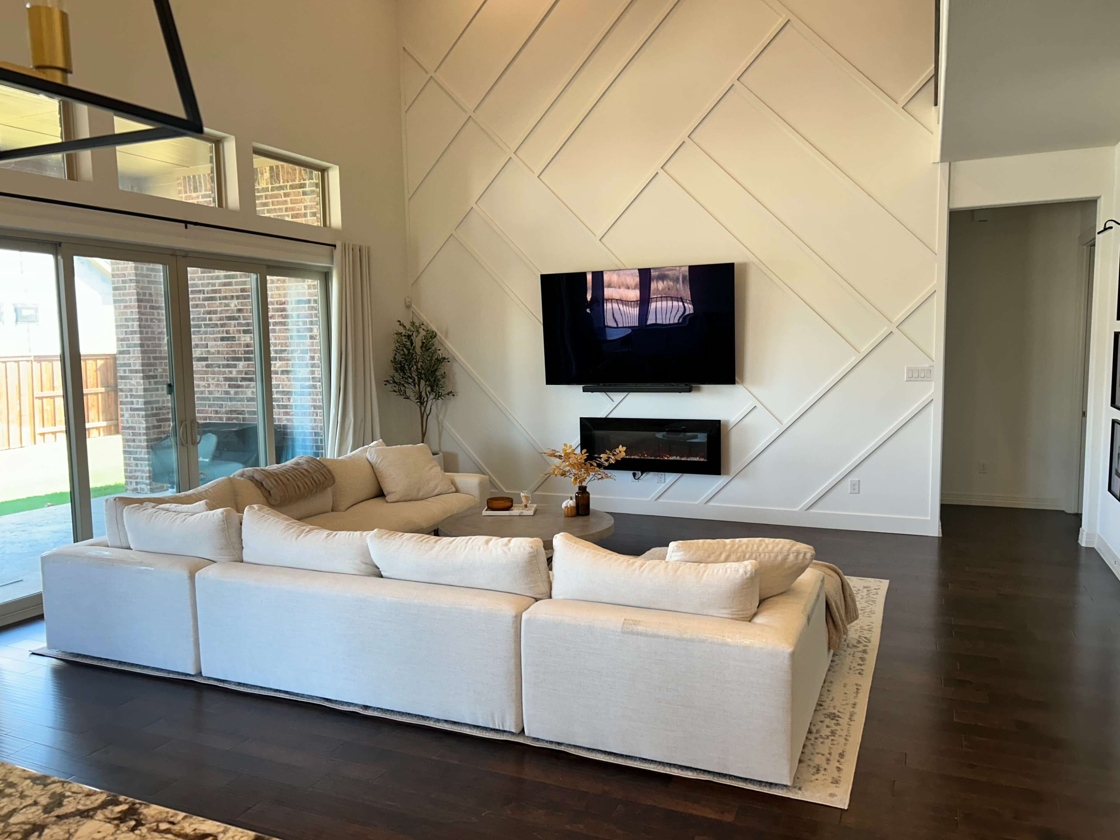 A spacious living room features a large sectional sofa, a wall-mounted television, and a modern electric fireplace.