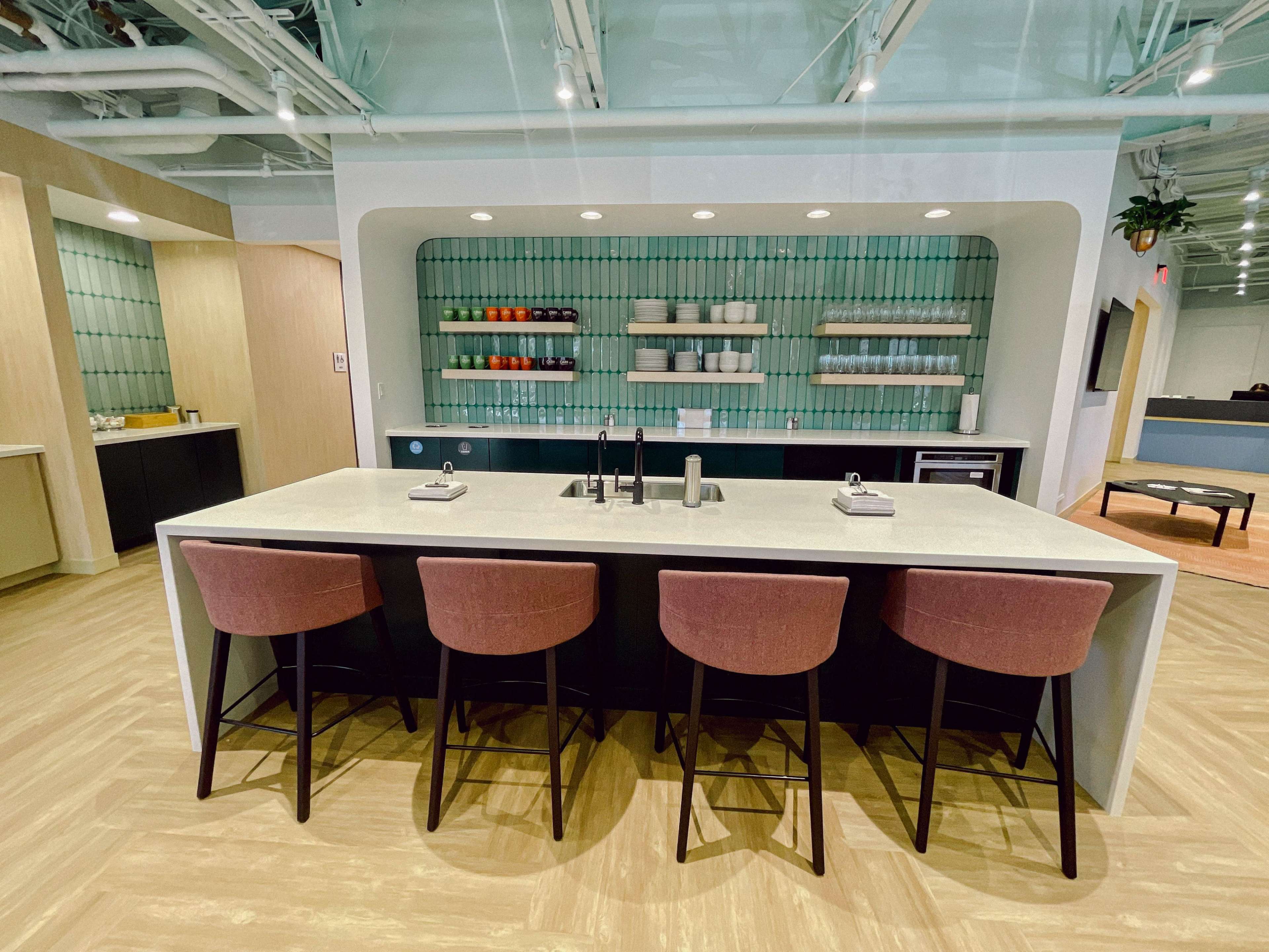 A modern kitchen area with a large island, four stool seats, and wall-mounted shelves displaying various dishes and cups.