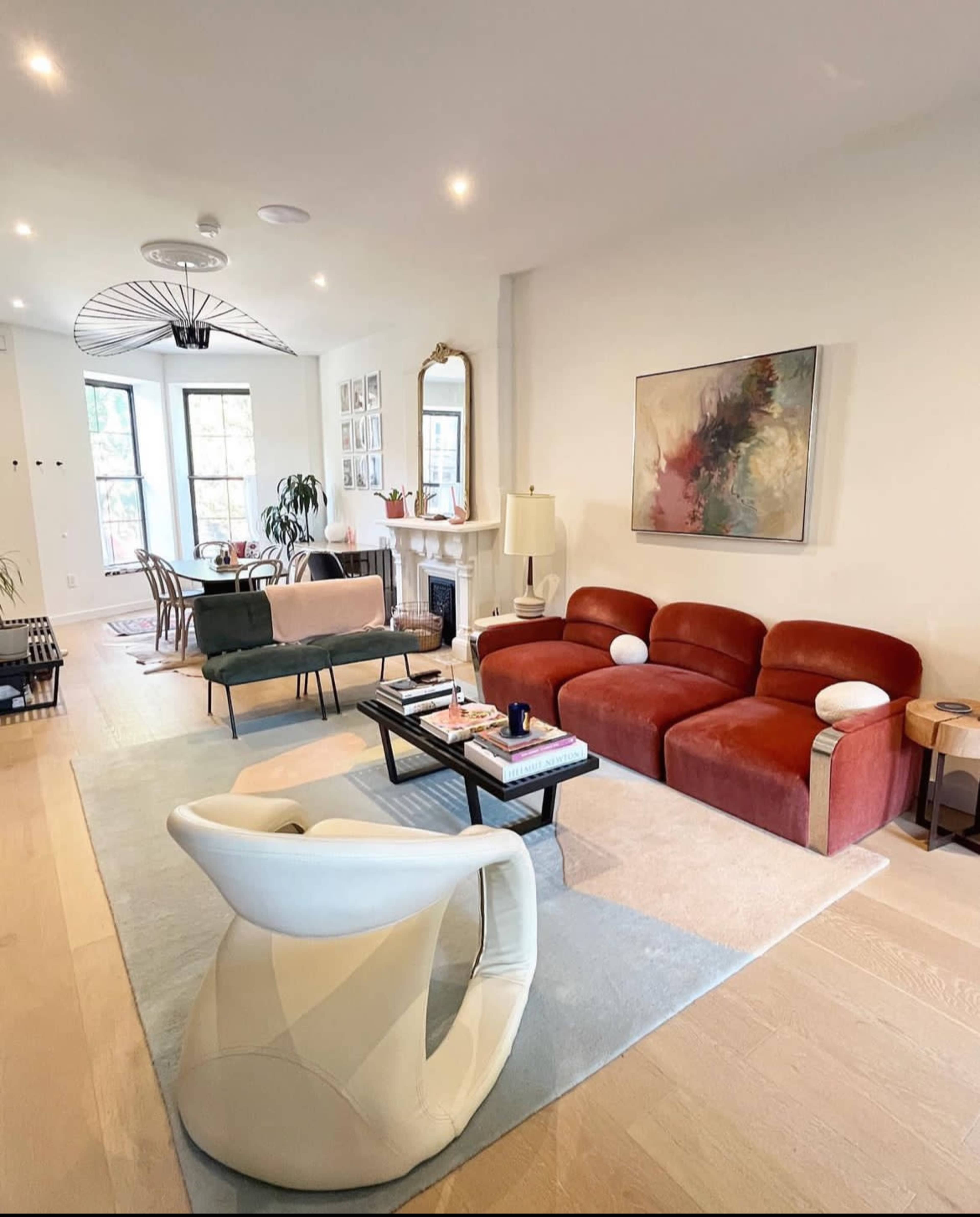 The living room features a mix of seating areas, including a red three-seat sofa, a beige two-seat sofa, and a unique white armchair, arranged around a coffee table on a light rug.
