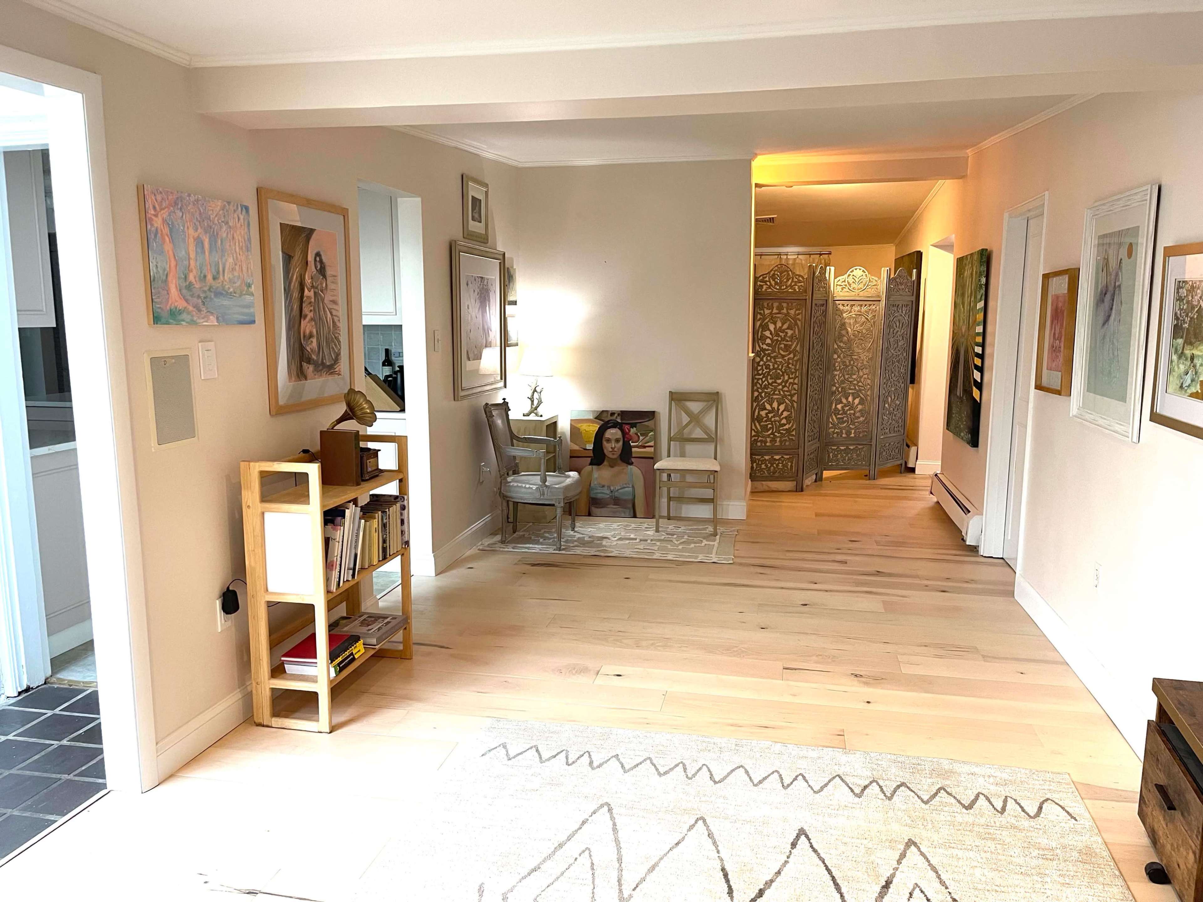 A spacious hallway featuring art on the walls, a bookshelf, a small table with chairs, and a decorative screen dividing the space.