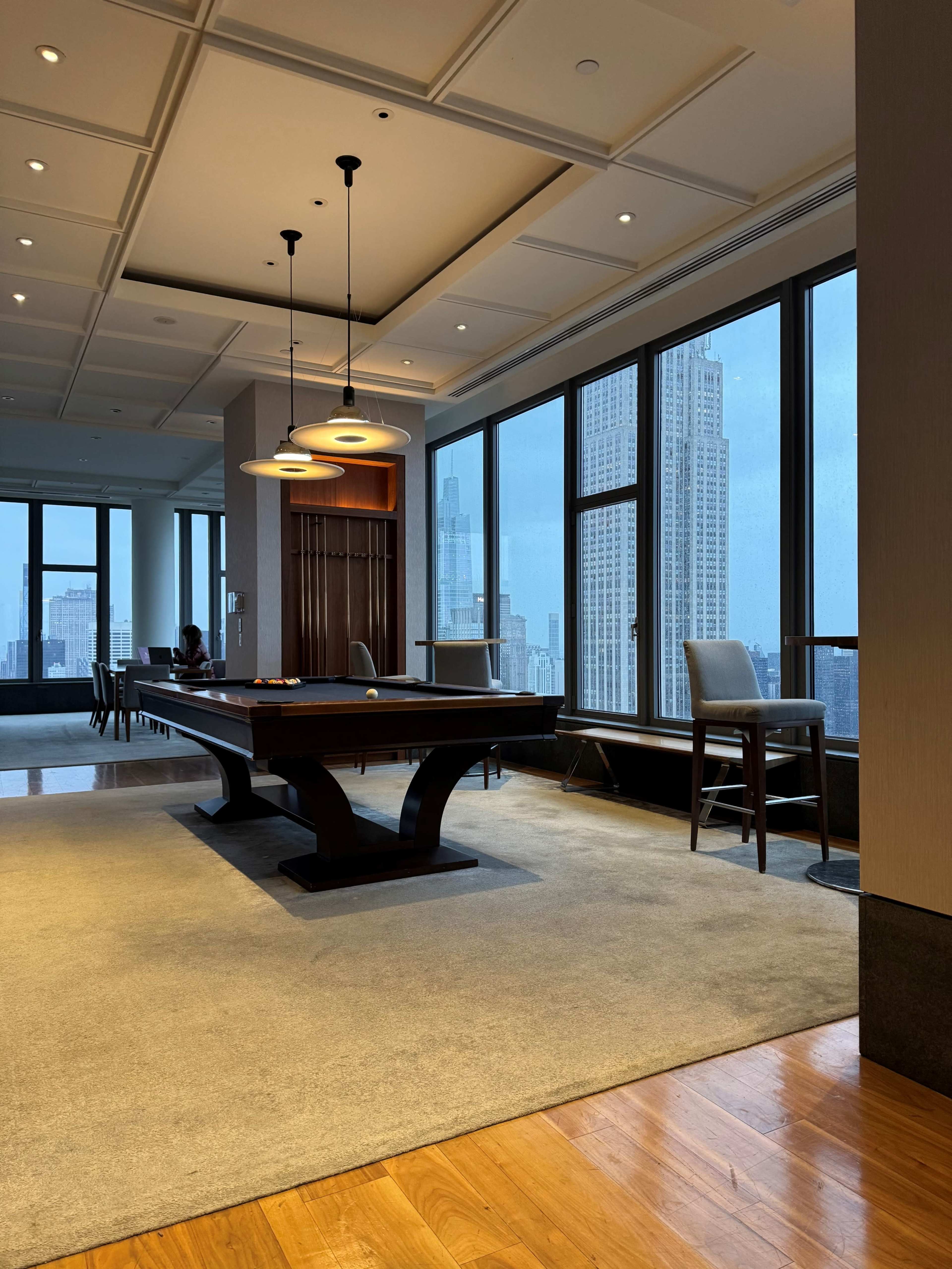 A modern game room featuring a pool table, large windows with a city view, and contemporary seating.