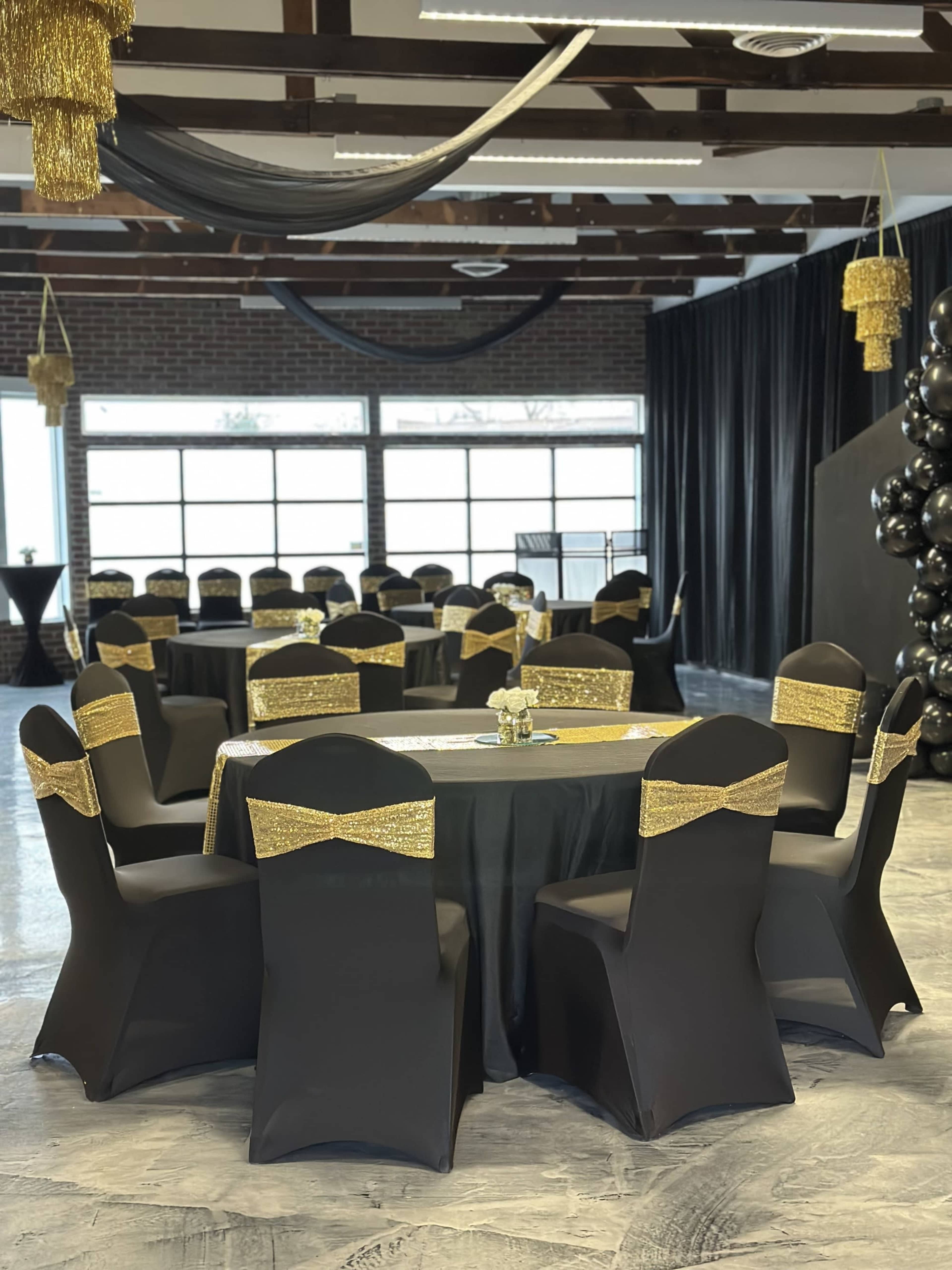 The image shows a banquet hall with black and gold themed decorations, featuring round tables covered in black tablecloths and chairs adorned with gold bow ties.