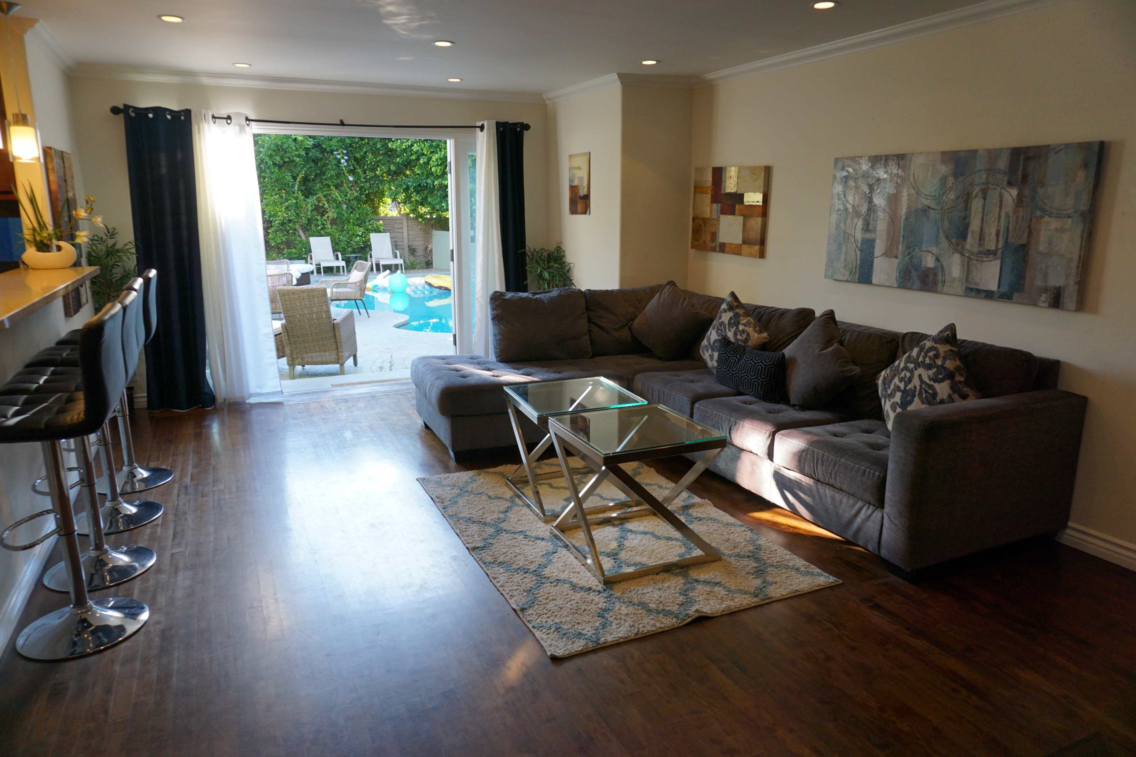 A cozy living room features a gray sectional sofa, a glass coffee table, and a view of a backyard pool through sliding glass doors.