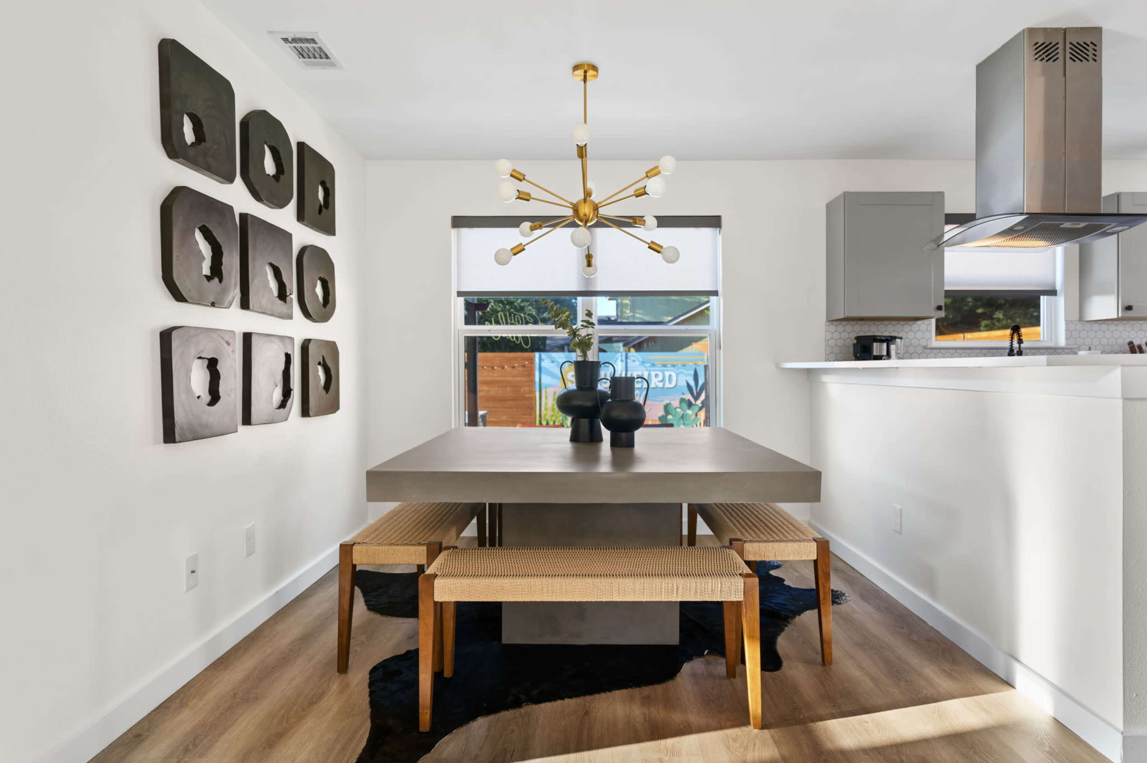 A modern dining room features a concrete table with two wooden benches, surrounded by wall art and a stylish light fixture.