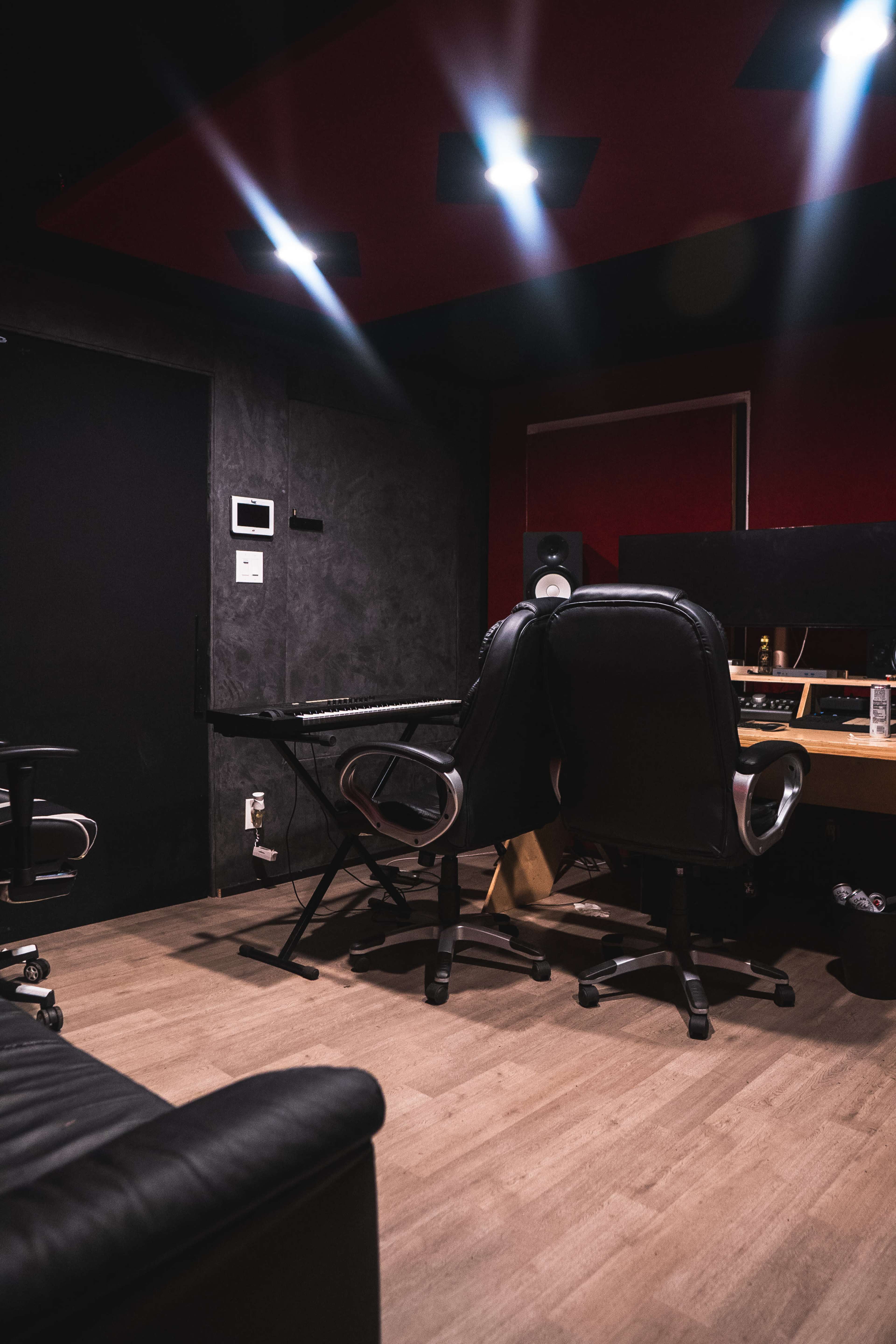 A dimly lit recording studio with a keyboard, two office chairs, and sound equipment against a wall.