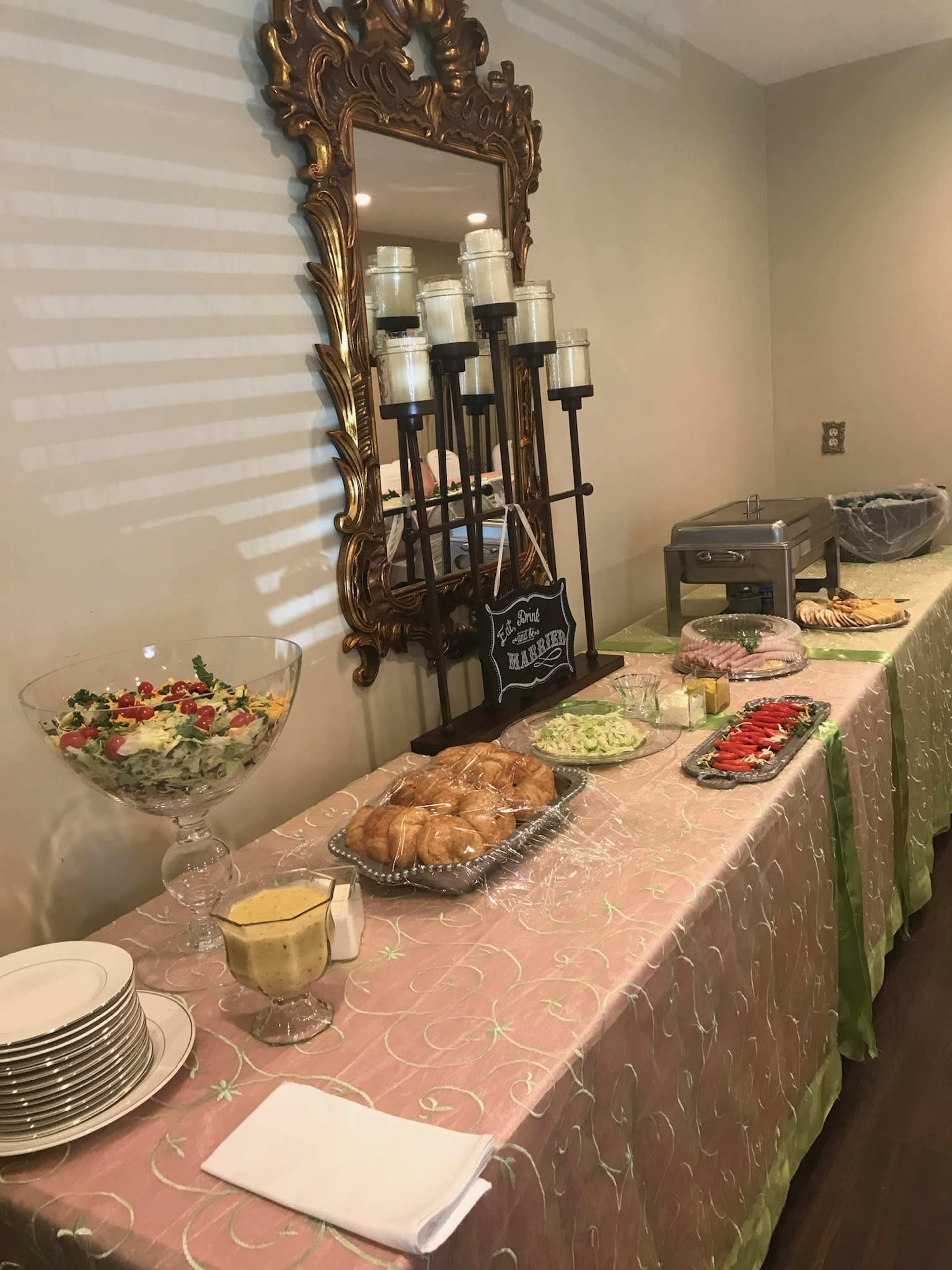 A buffet table is set up with a variety of food items, including salad, sandwiches, and pastries, alongside decorative candles and plates.