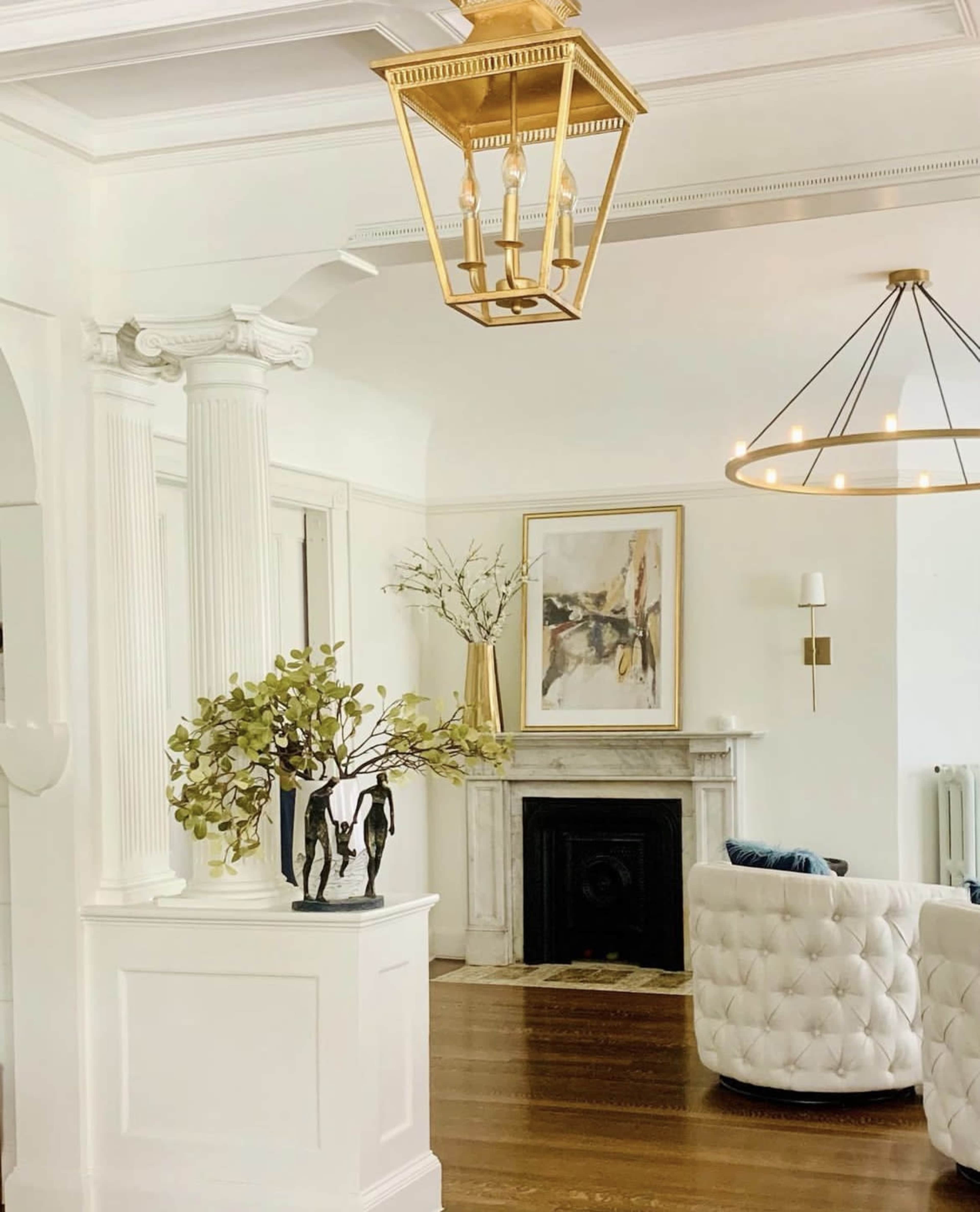 The image shows a bright, spacious living room featuring a decorative lantern, a marble fireplace, and a modern tufted sofa.