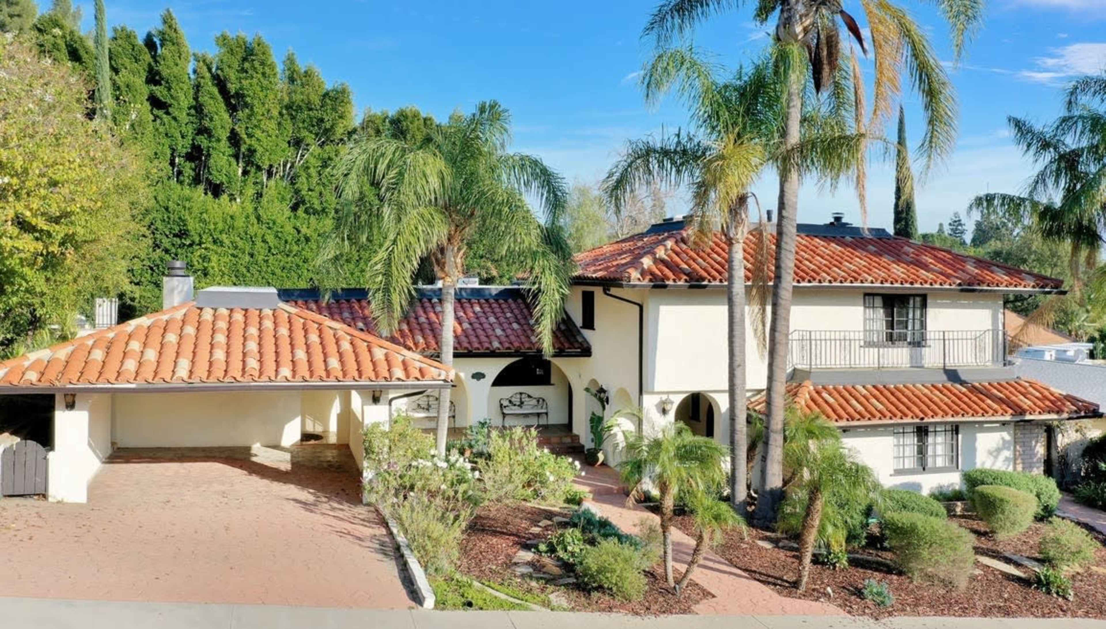 A two-story house with a terracotta roof surrounded by palm trees and landscaped gardens.