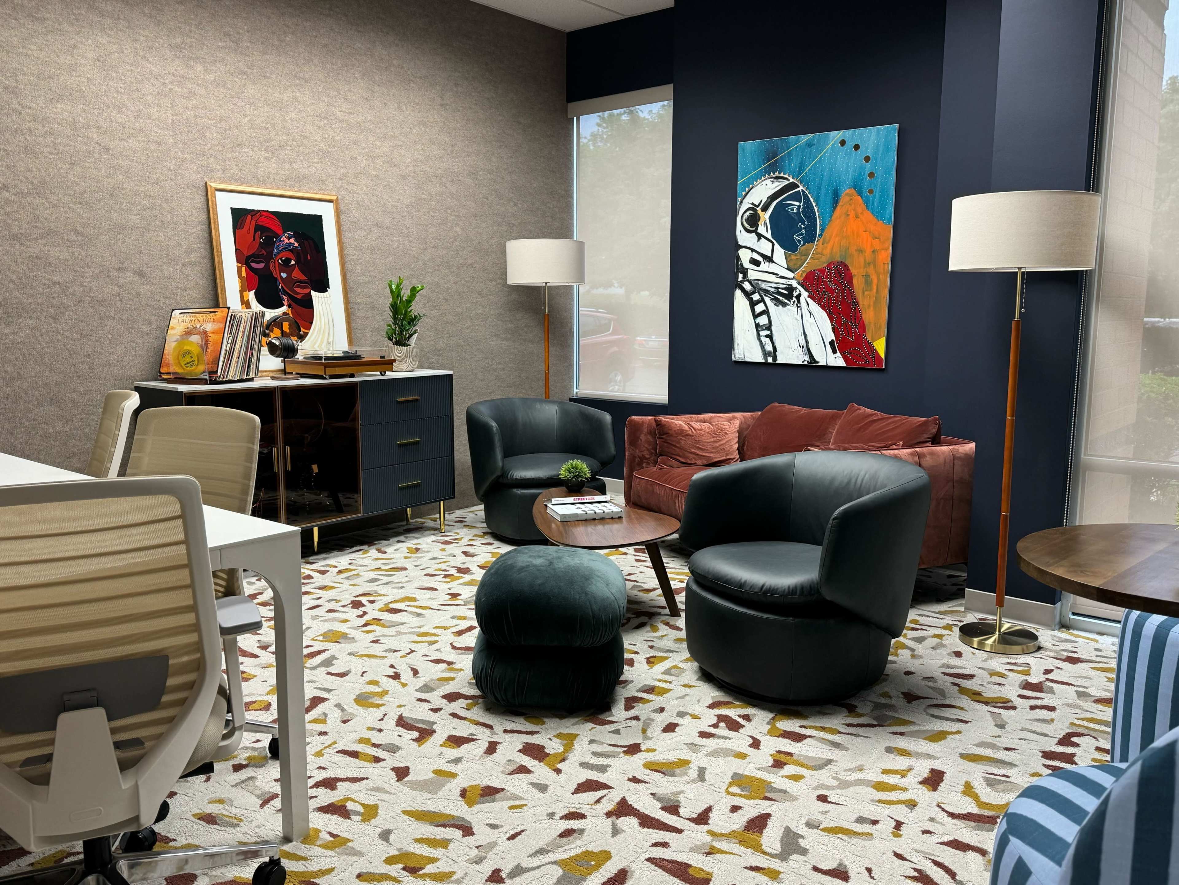 A modern office space featuring a seating area with a red couch, black chairs, a round table, and a colorful artwork of an astronaut on the wall.
