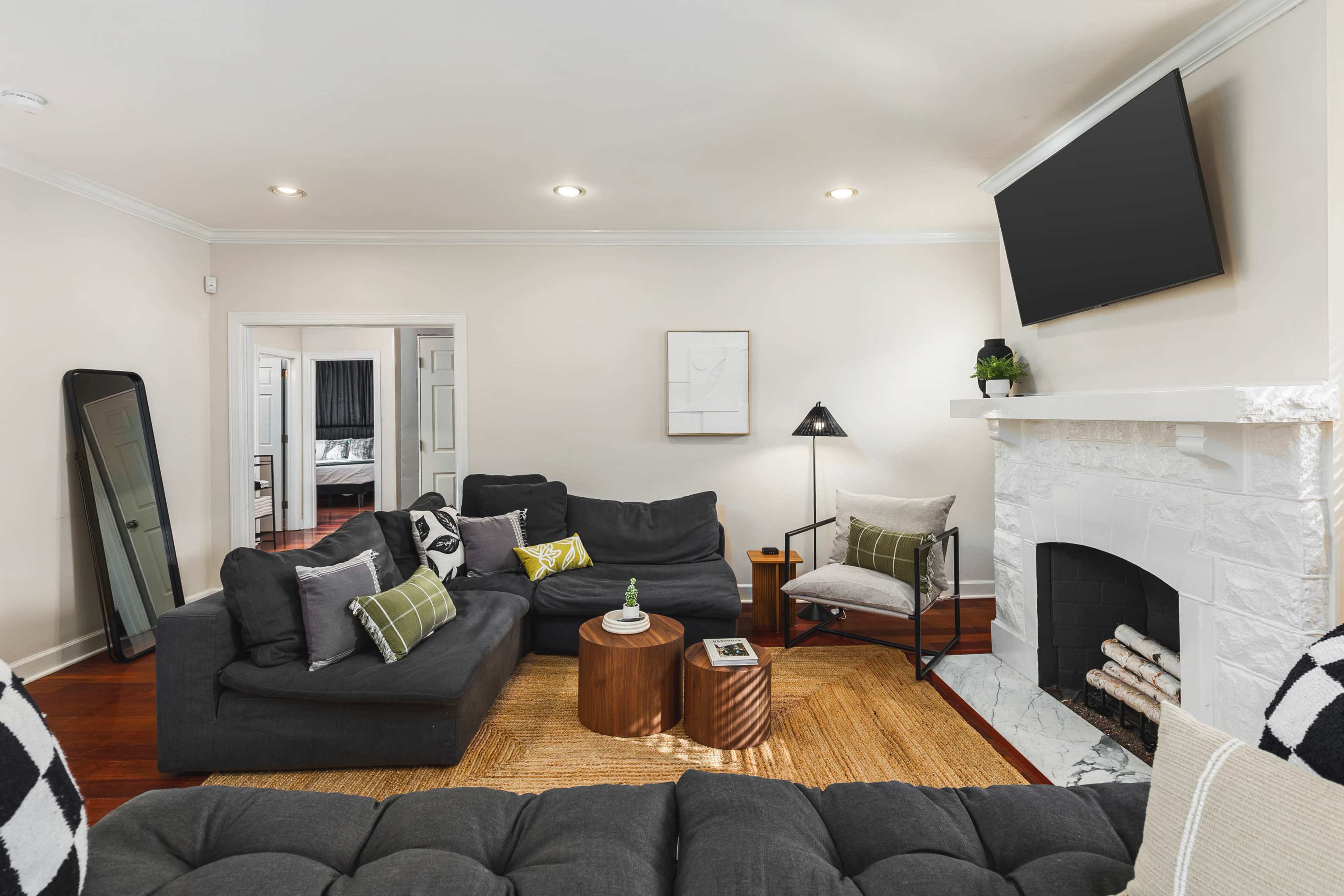 A modern living room features a sectional sofa, two wooden side tables, a marble fireplace, and a flat-screen TV mounted on the wall.