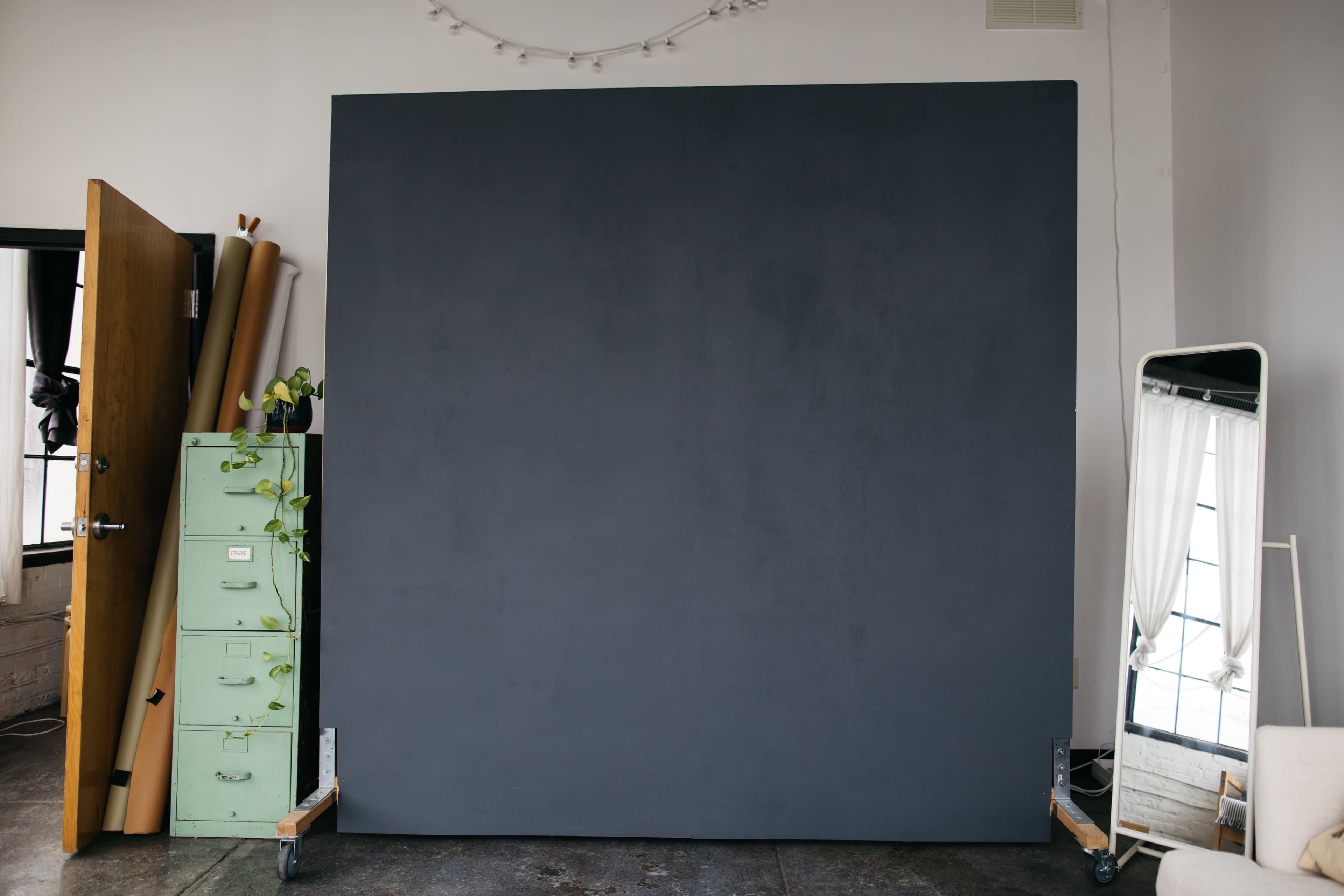 The image shows a large gray backdrop positioned in a room with an open door, a mirror, and a green filing cabinet.