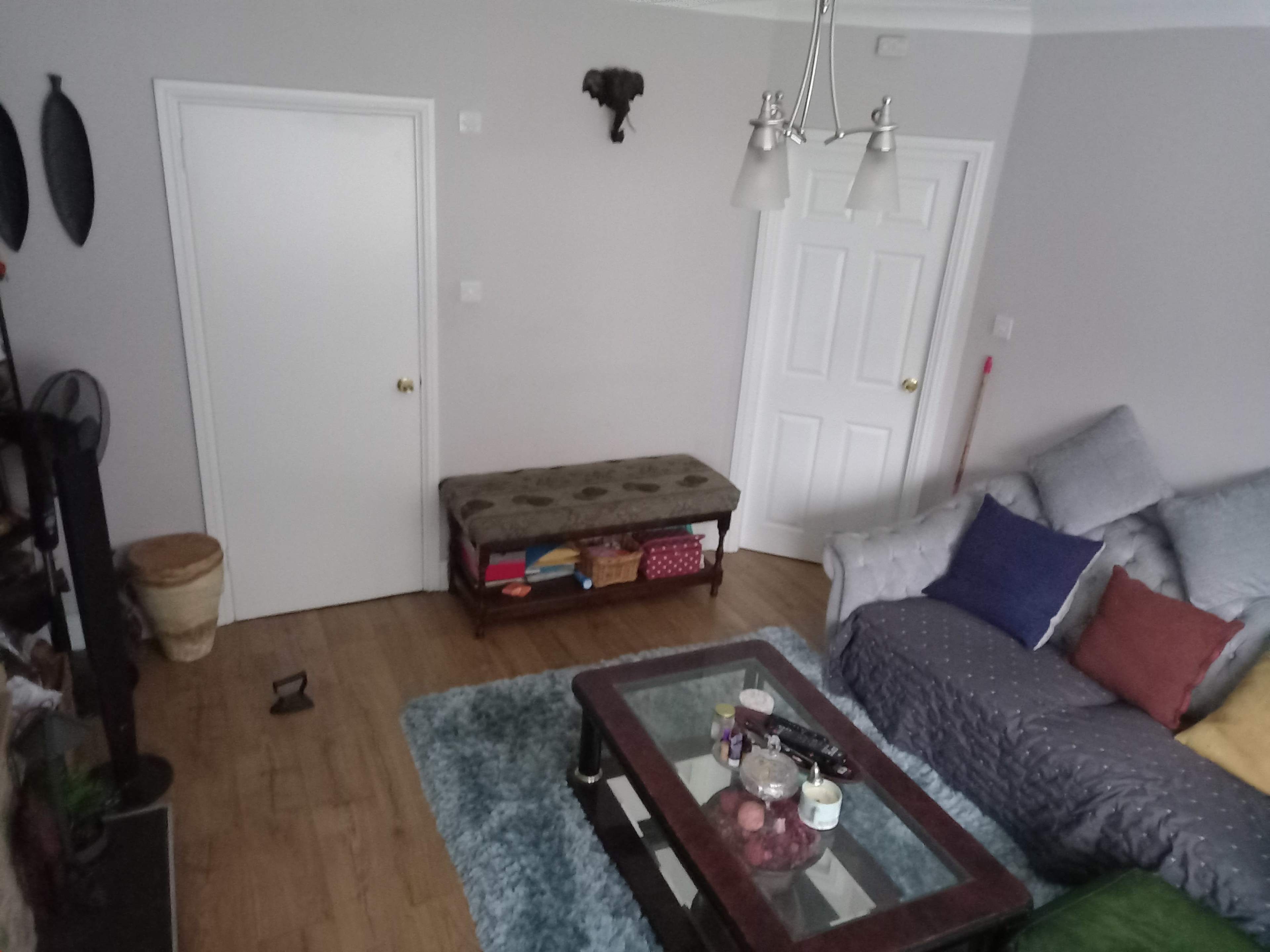 A living room with a couch adorned with colorful cushions, a wooden coffee table, and a closed door set against light-colored walls.