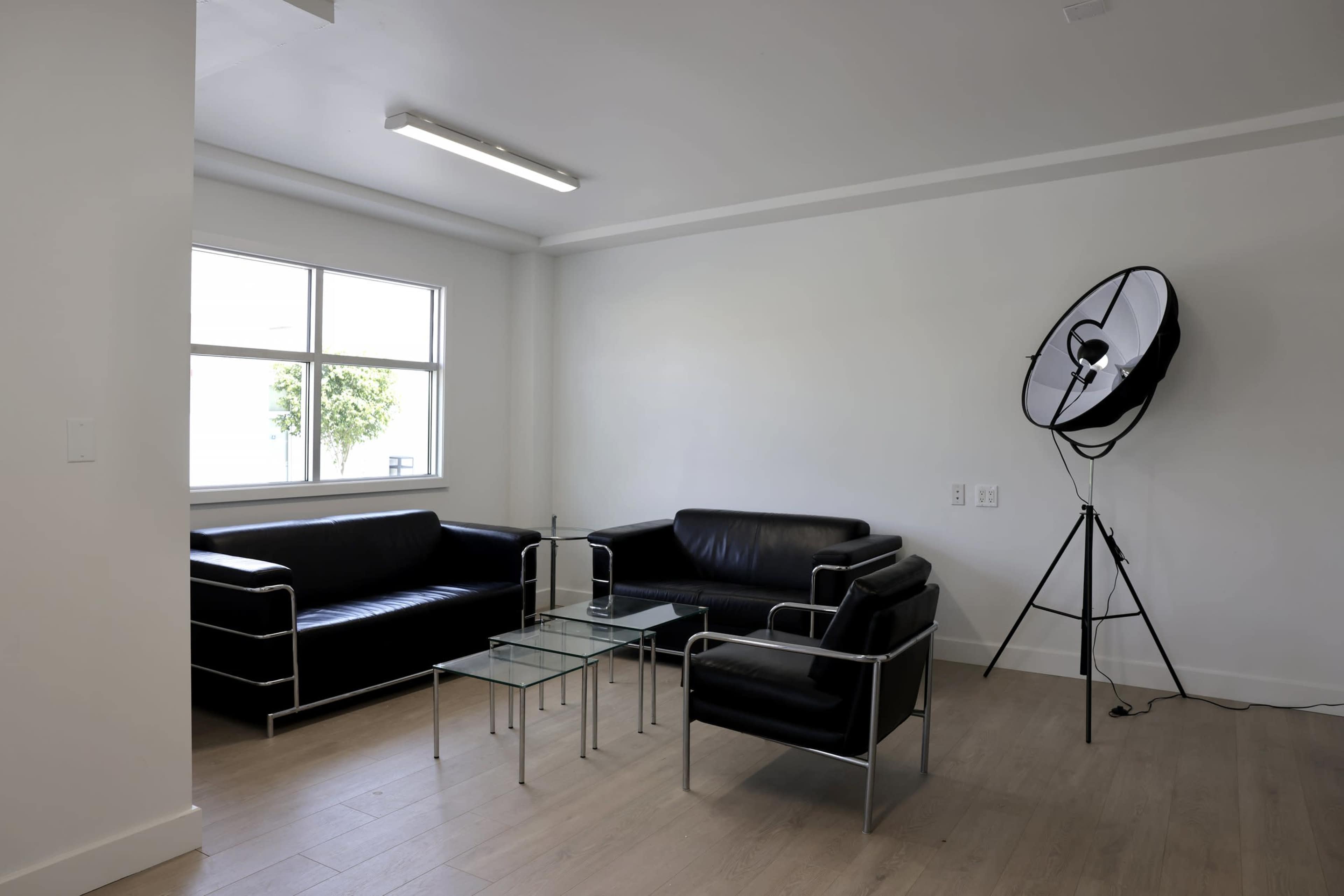 A modern living space features two black sofas, a glass coffee table, and a large floor lamp near a window.