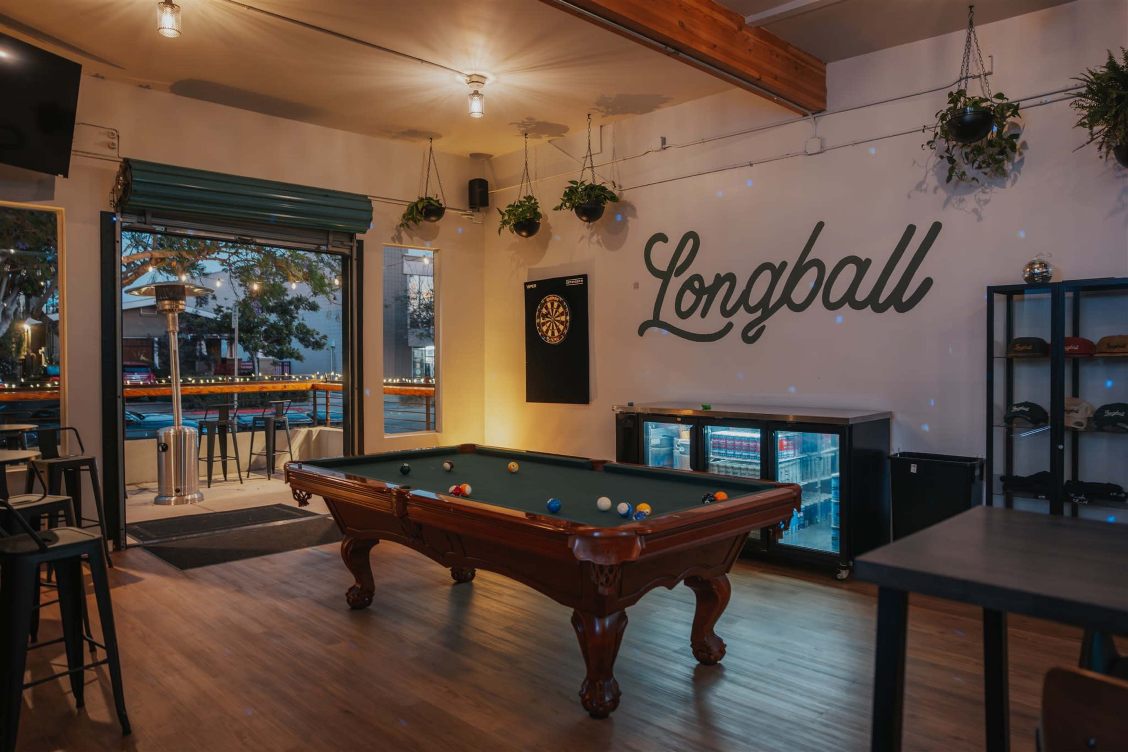 The image shows a bar area with a pool table in the center, surrounded by greenery and featuring a large sign that reads "Longball."