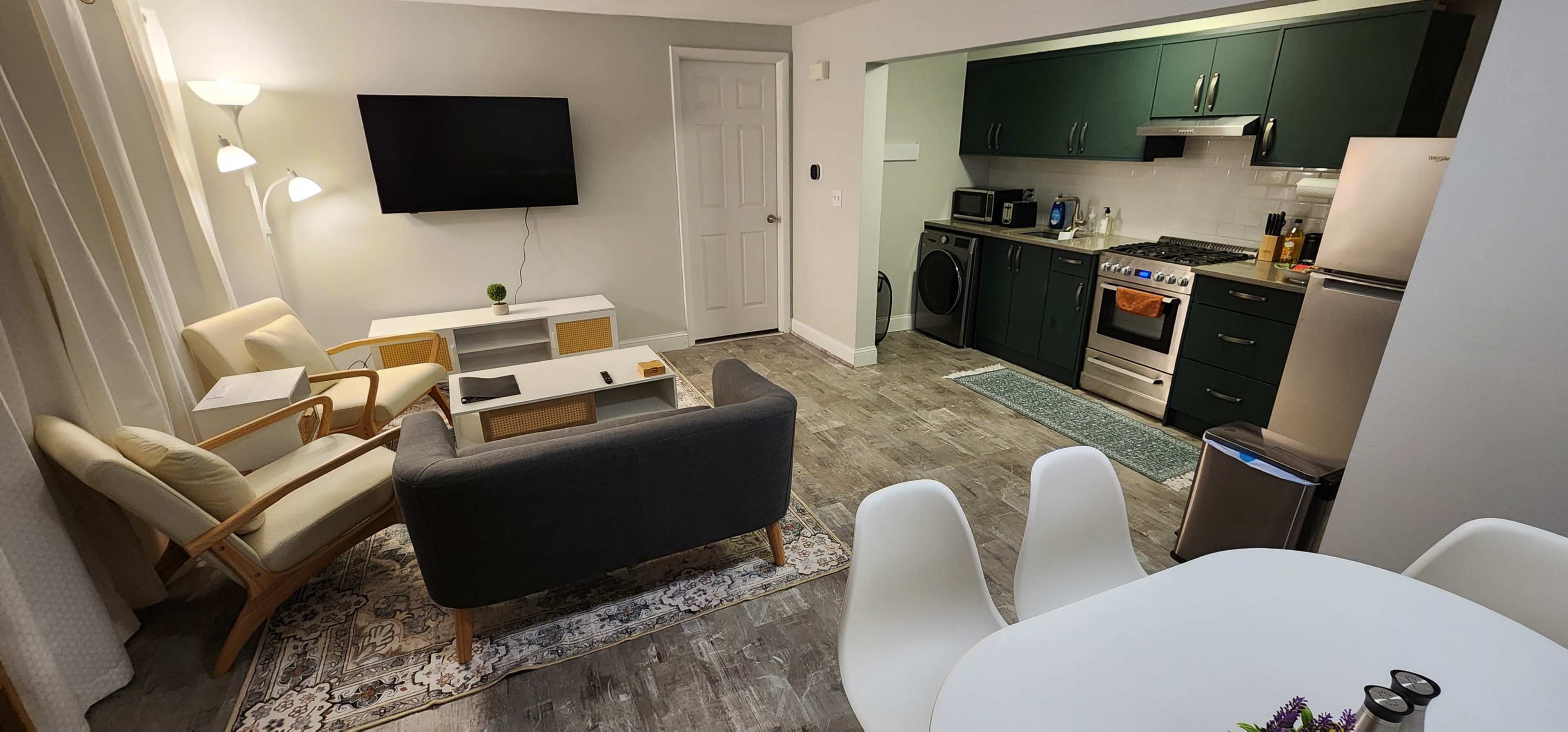 A modern interior of a living space featuring a kitchen with appliances, a dining area, and a cozy seating area with a gray sofa and light-colored furniture.