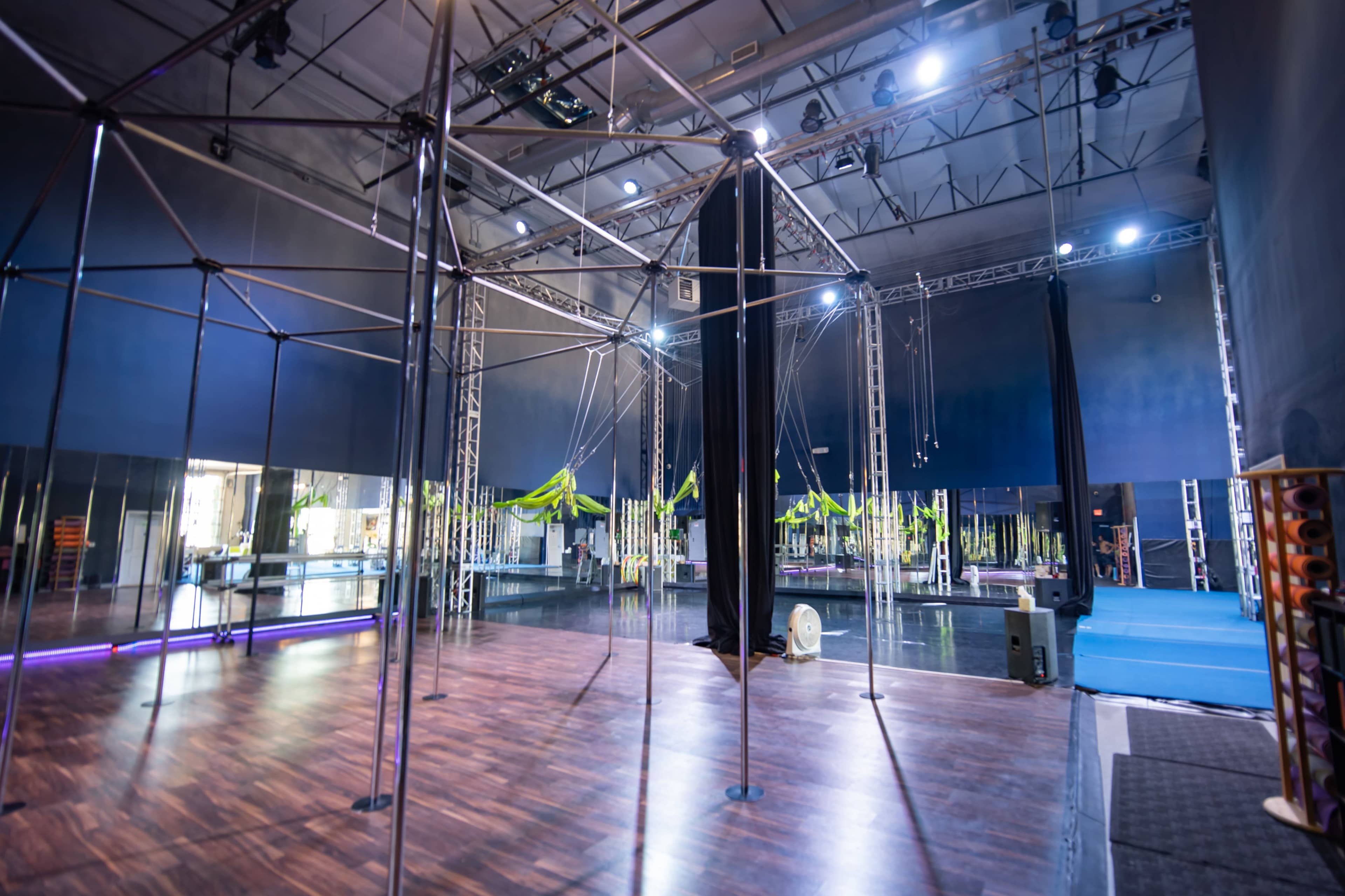A spacious, empty performance studio equipped with apparatuses for aerial arts, featuring mirrored walls and stage lighting.