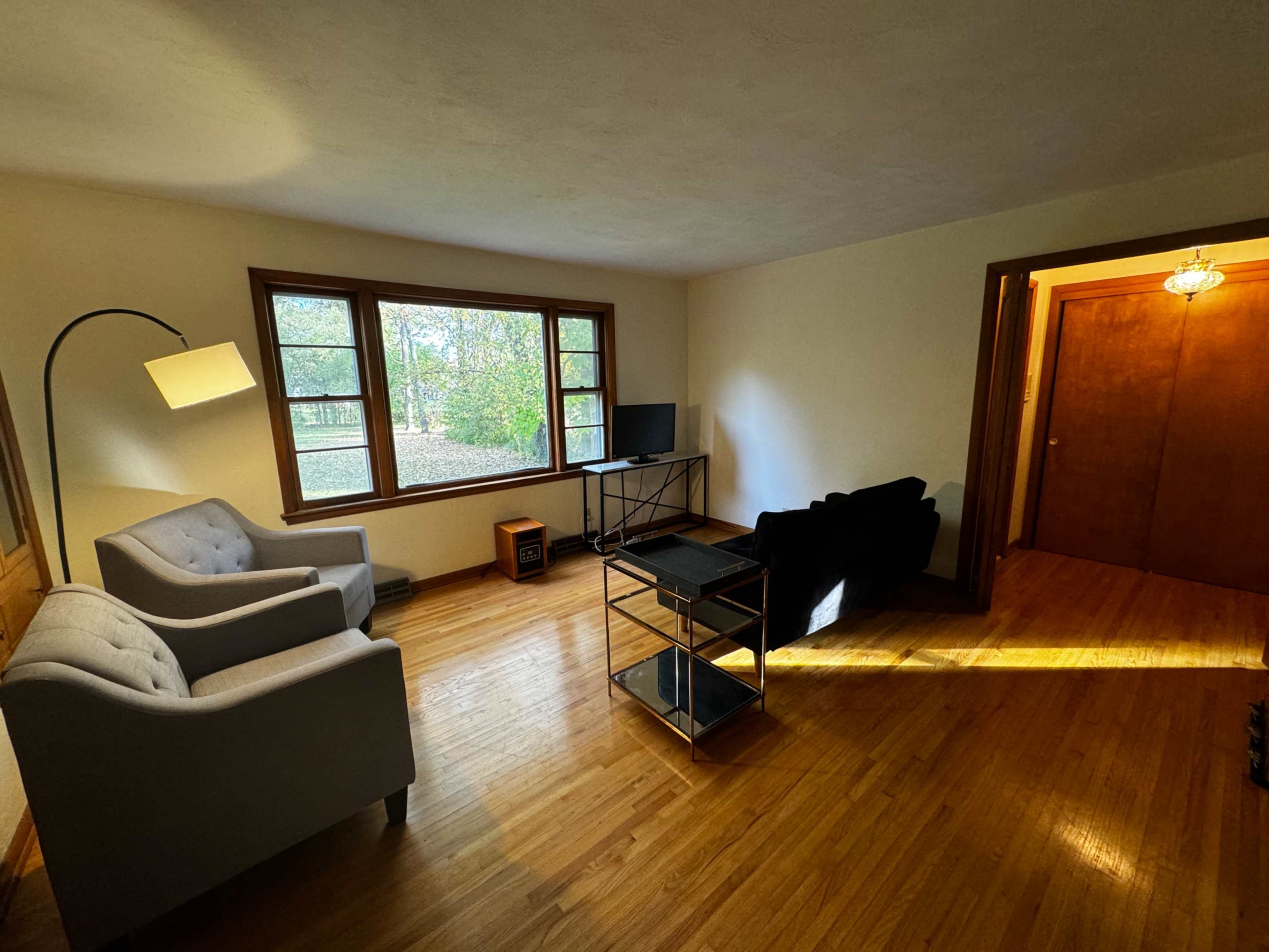 The room features two chairs, a small table, a television on a stand, and a large window with a view of the outdoors.