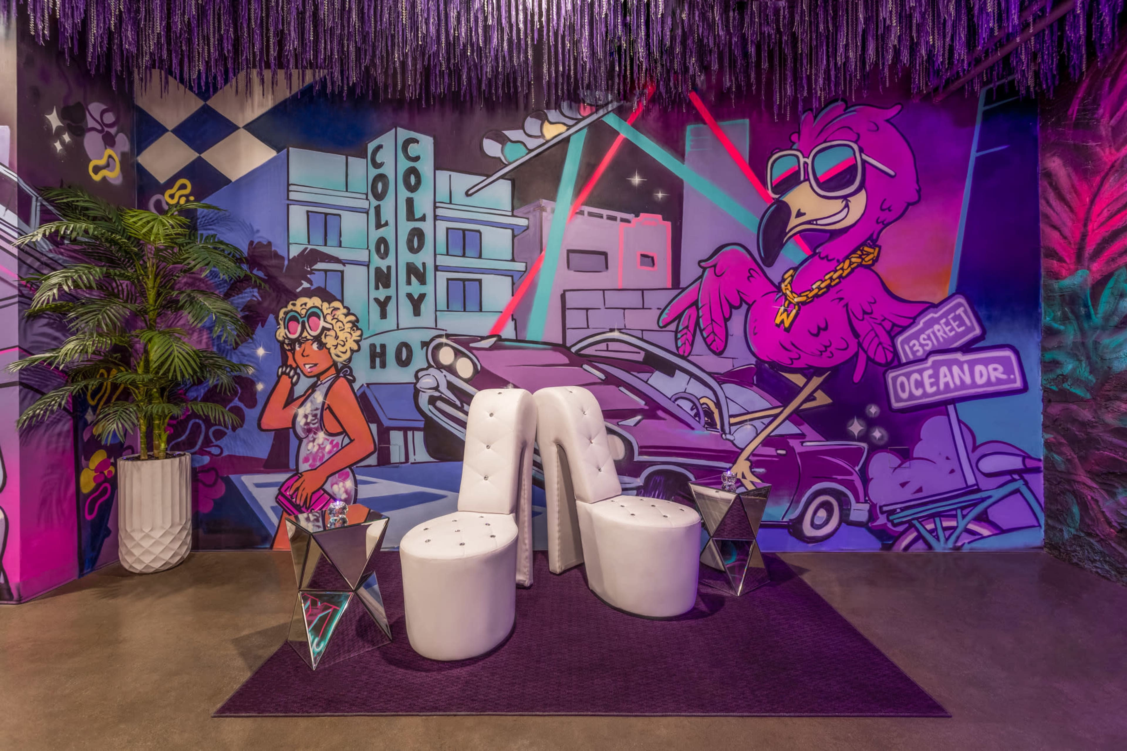A vibrant interior with colorful murals, including a stylized flamingo and a woman, alongside white modern seating and decorative plants.