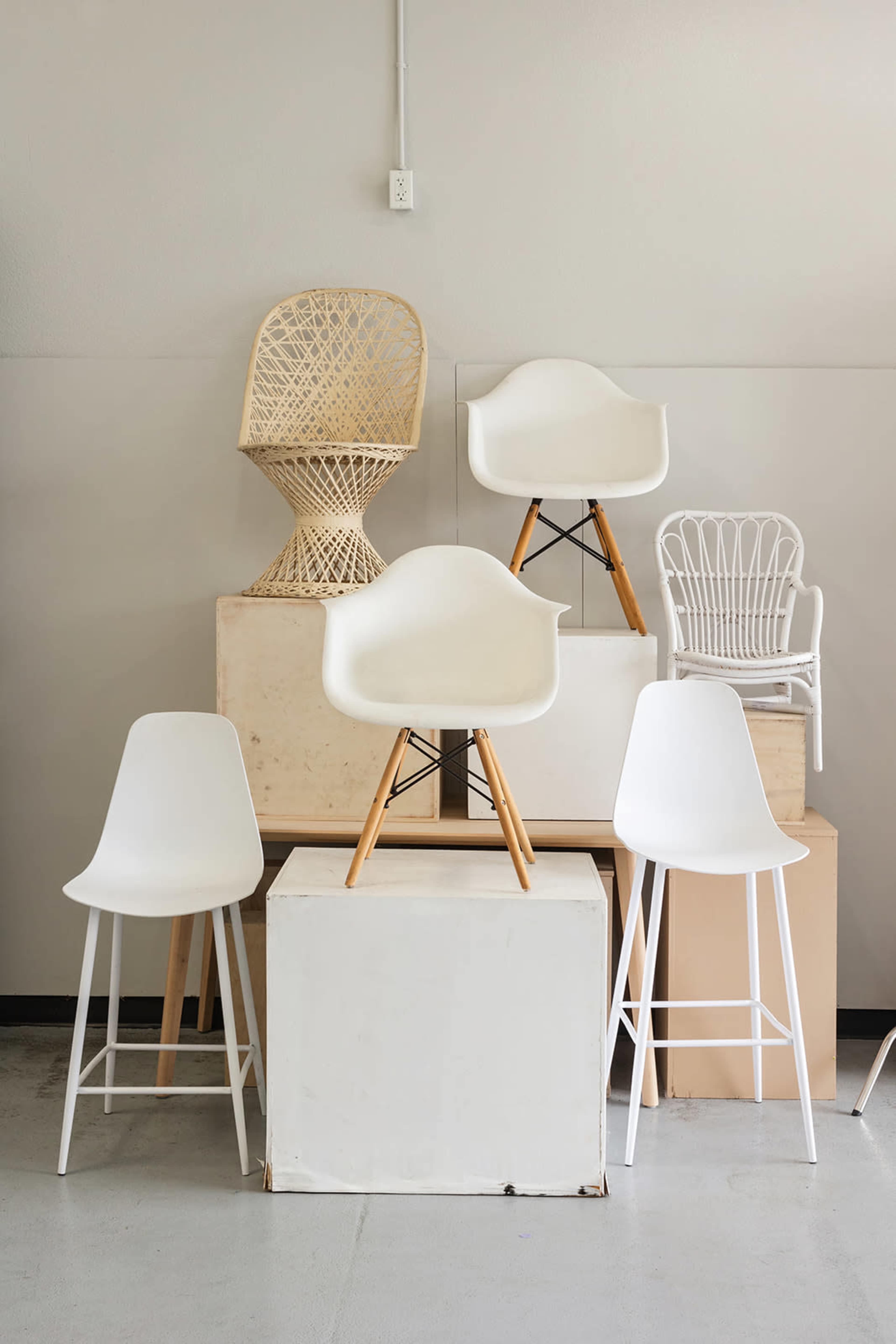 The image features a collection of chairs arranged on various surfaces, including white modern chairs, a rattan chair, and a small white wicker chair.