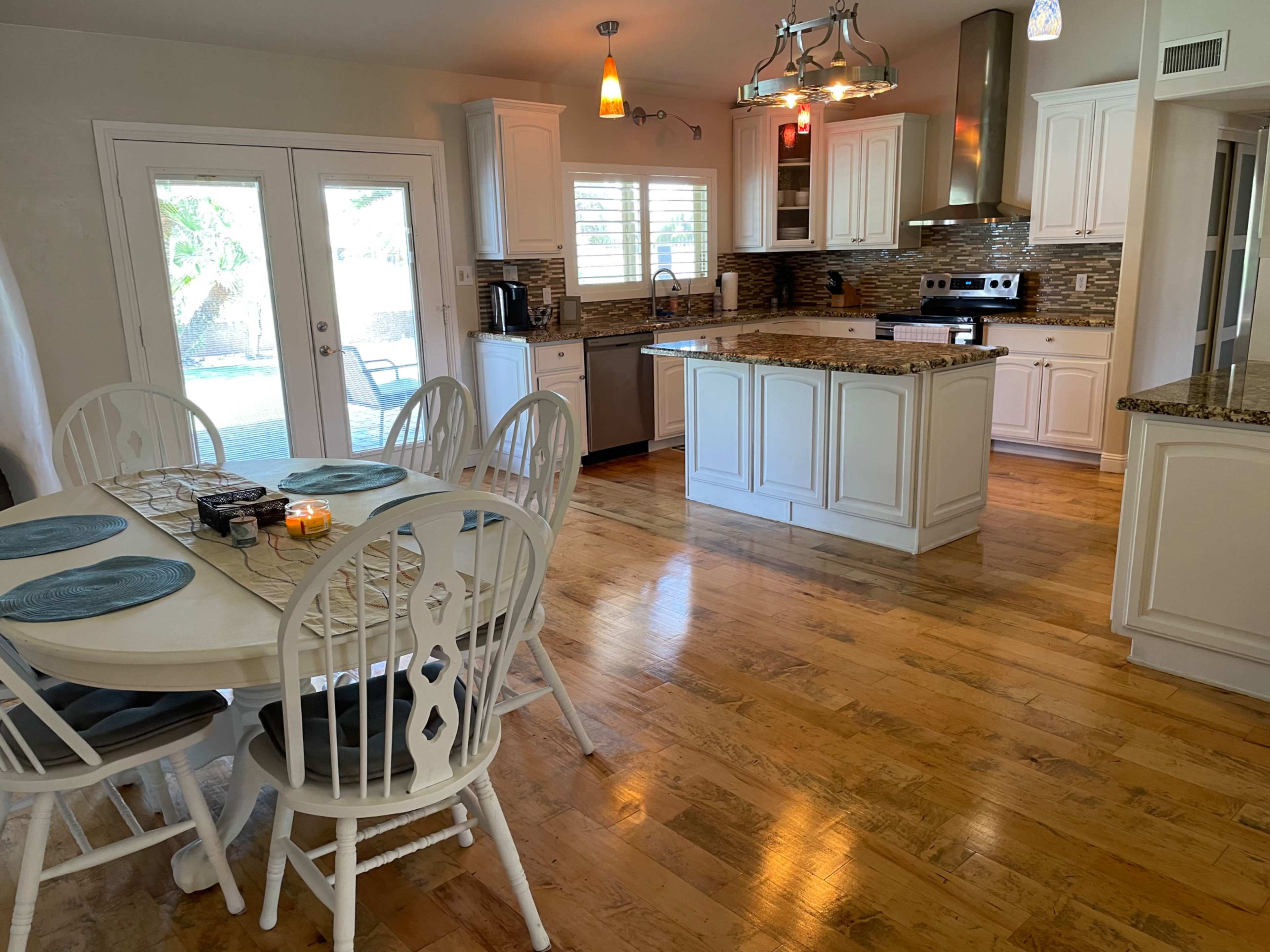 A bright kitchen and dining area with a round table set for six, featuring white cabinetry and granite countertops.
